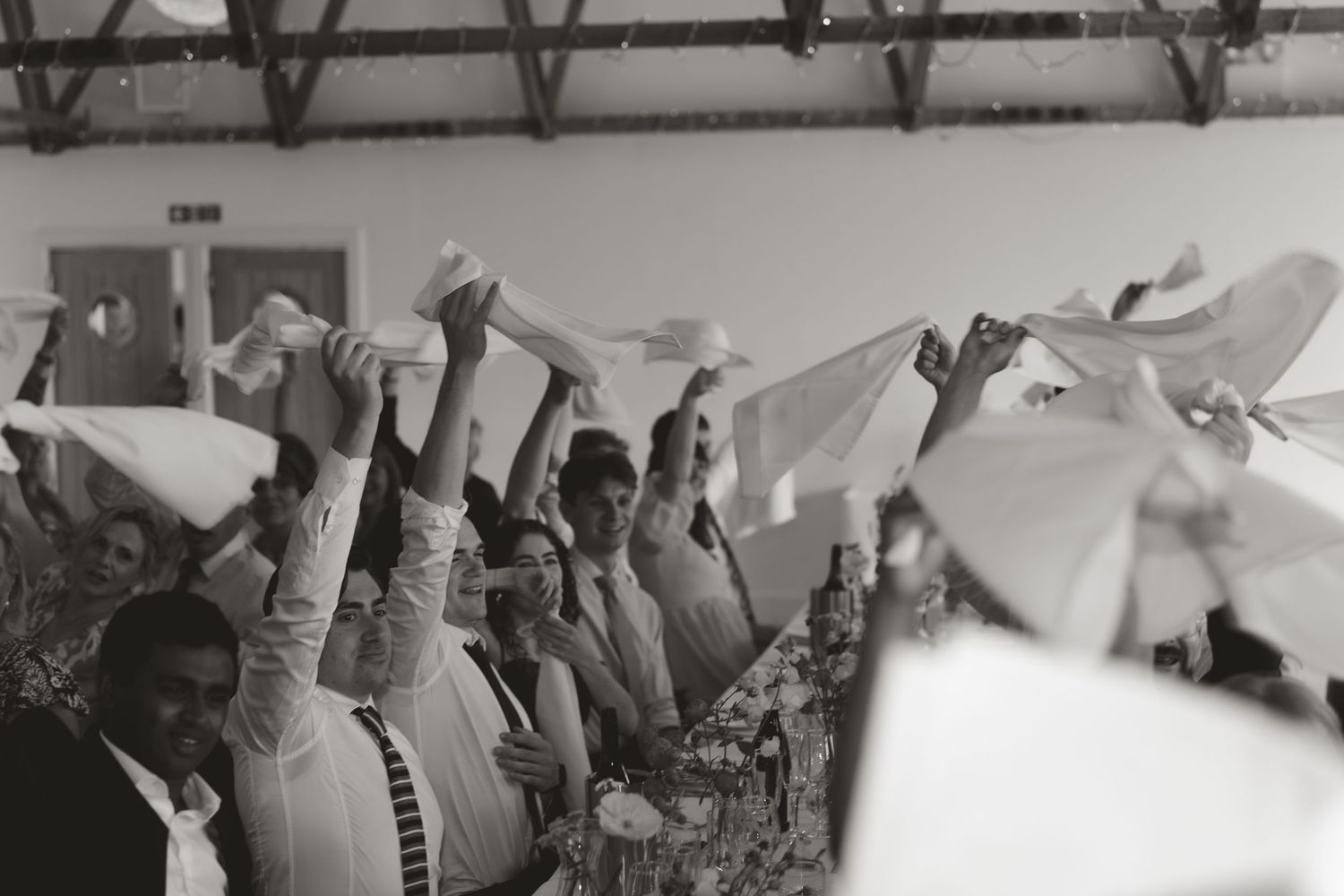 Black and white image of wedding guests raising hands in celebration.
