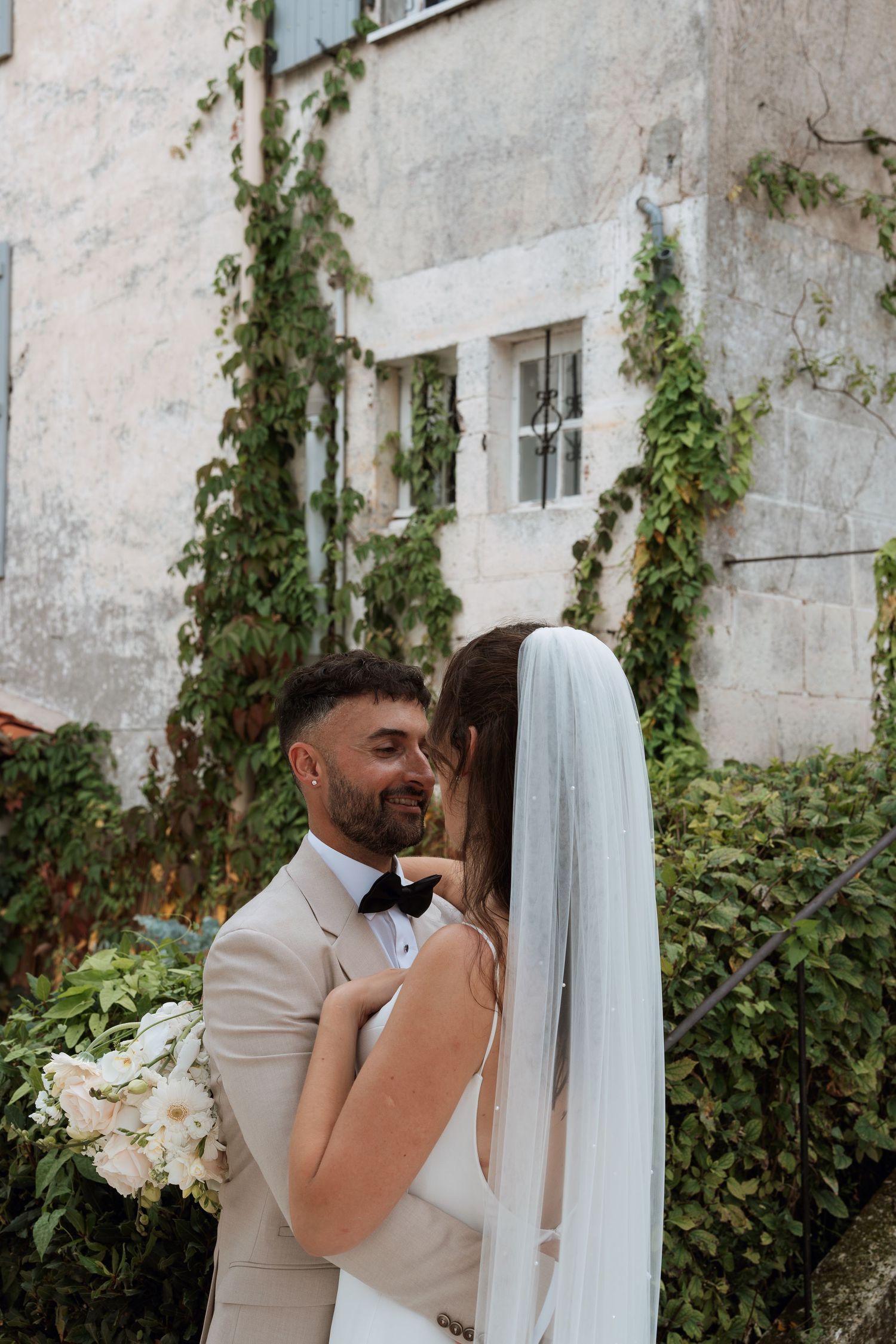 Romantic wedding photos against an ivy-covered wall with flowing white veil.