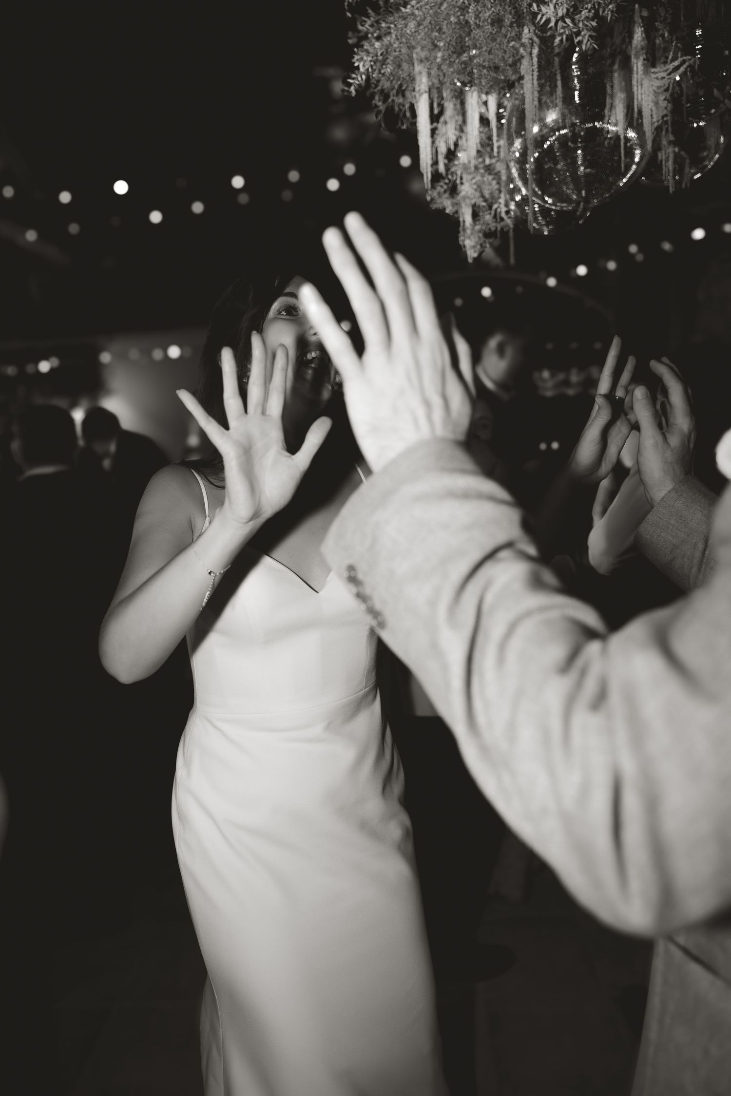 People dancing with raised hands under twinkling lights at a nighttime celebration.