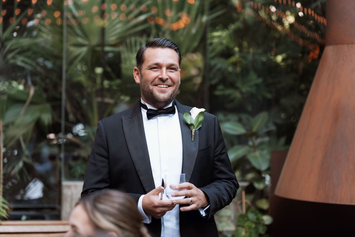 A person in formal attire holding a drink outdoors at an event.