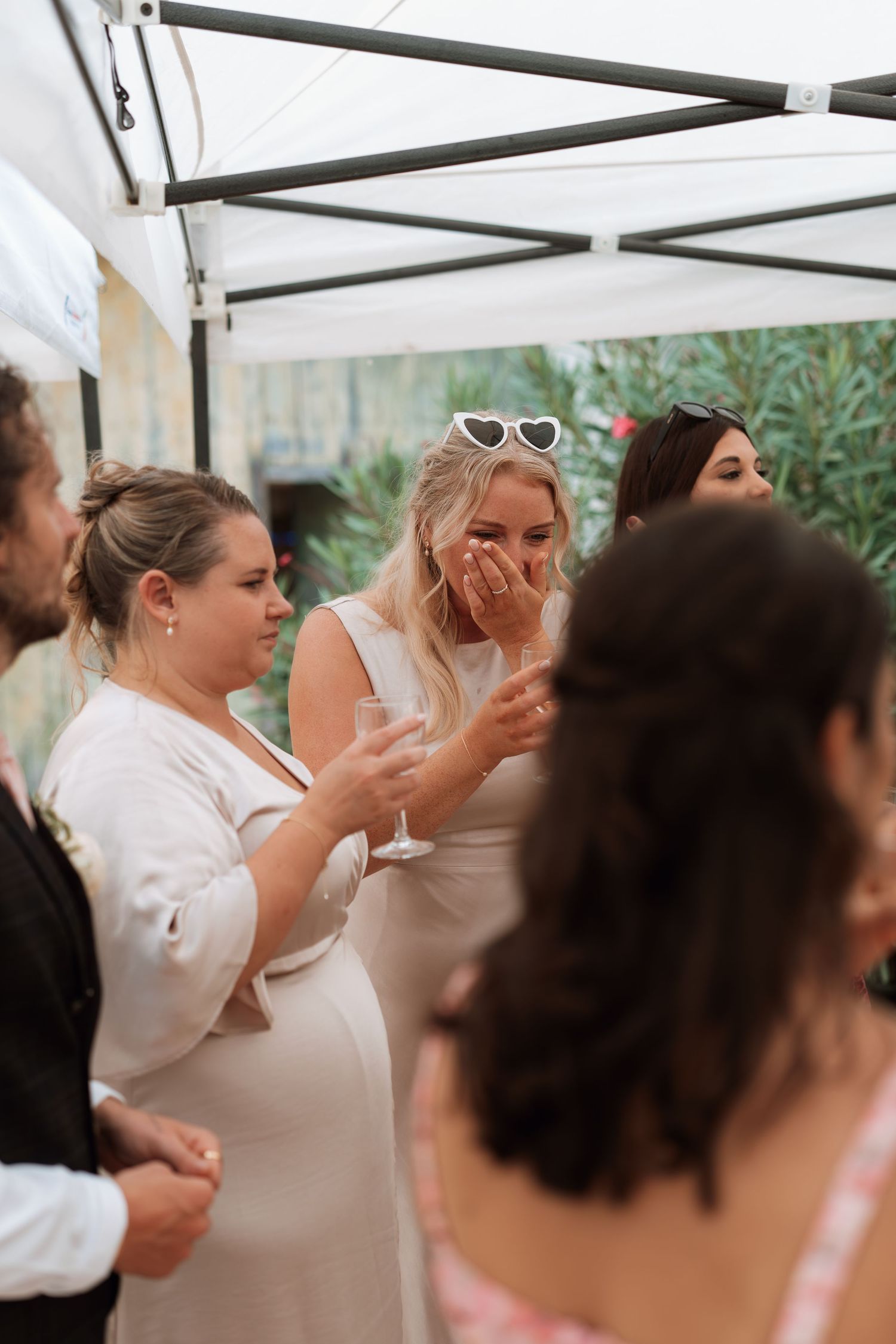 Wedding guests in white attire celebrating under outdoor tent.