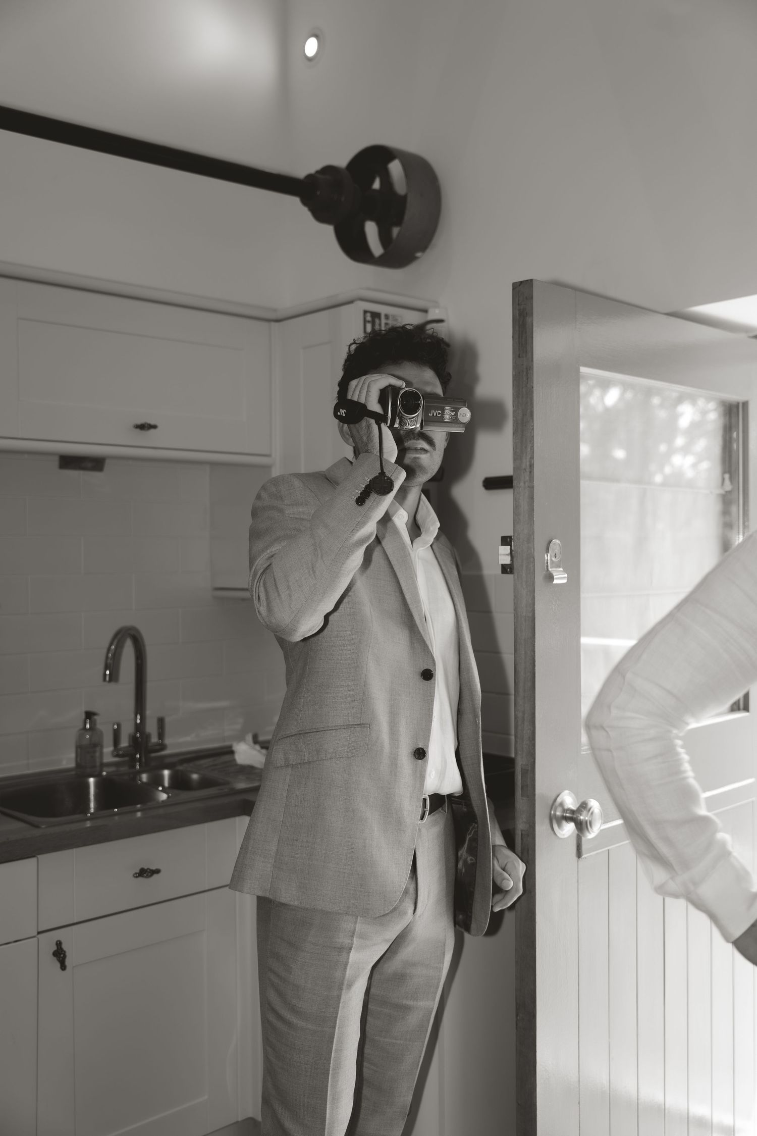 Wedding photographer in light gray suit taking photos in indoor setting.