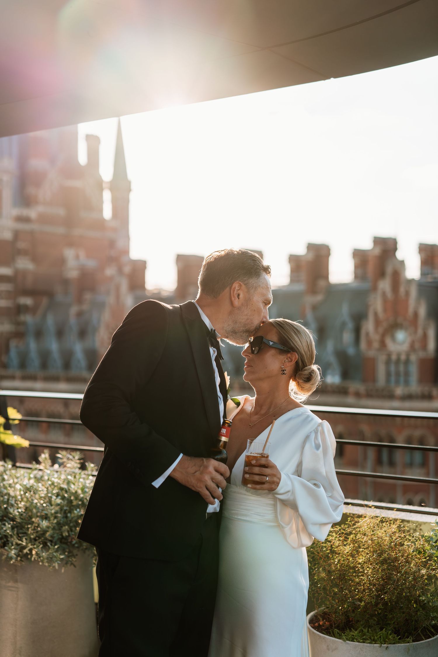 Newlyweds share an intimate moment at sunset on a city rooftop.