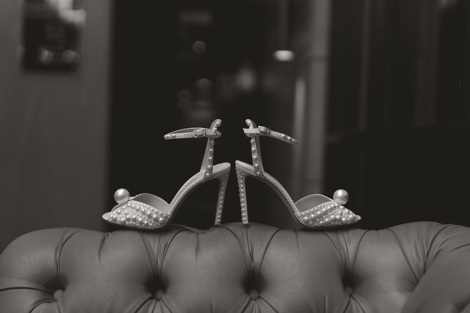 Elegant silver bridal shoes with crystal embellishments displayed on a gray tufted couch.
