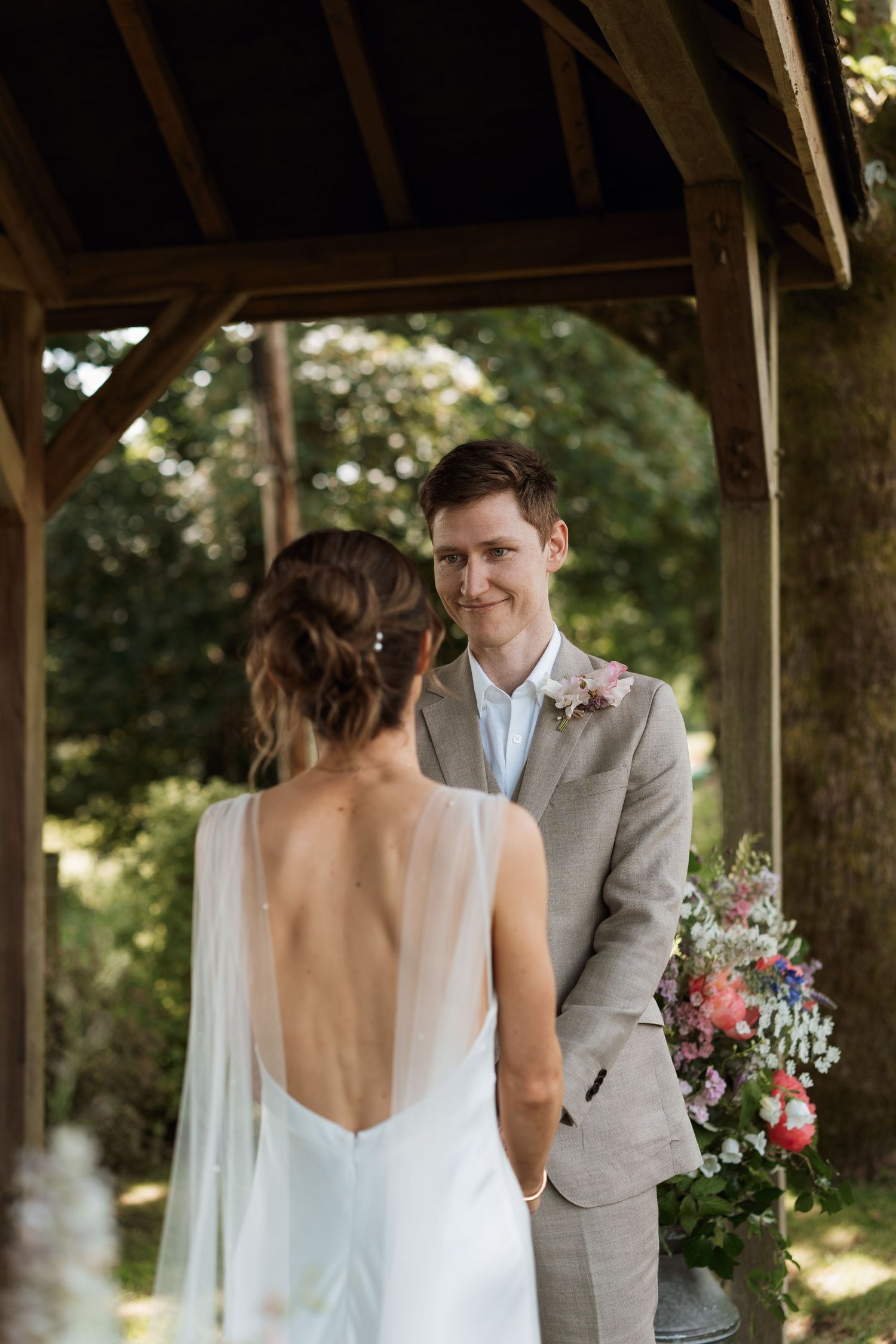 Couple sharing a romantic moment under a wooden pavilion decorated with floral arrangements.