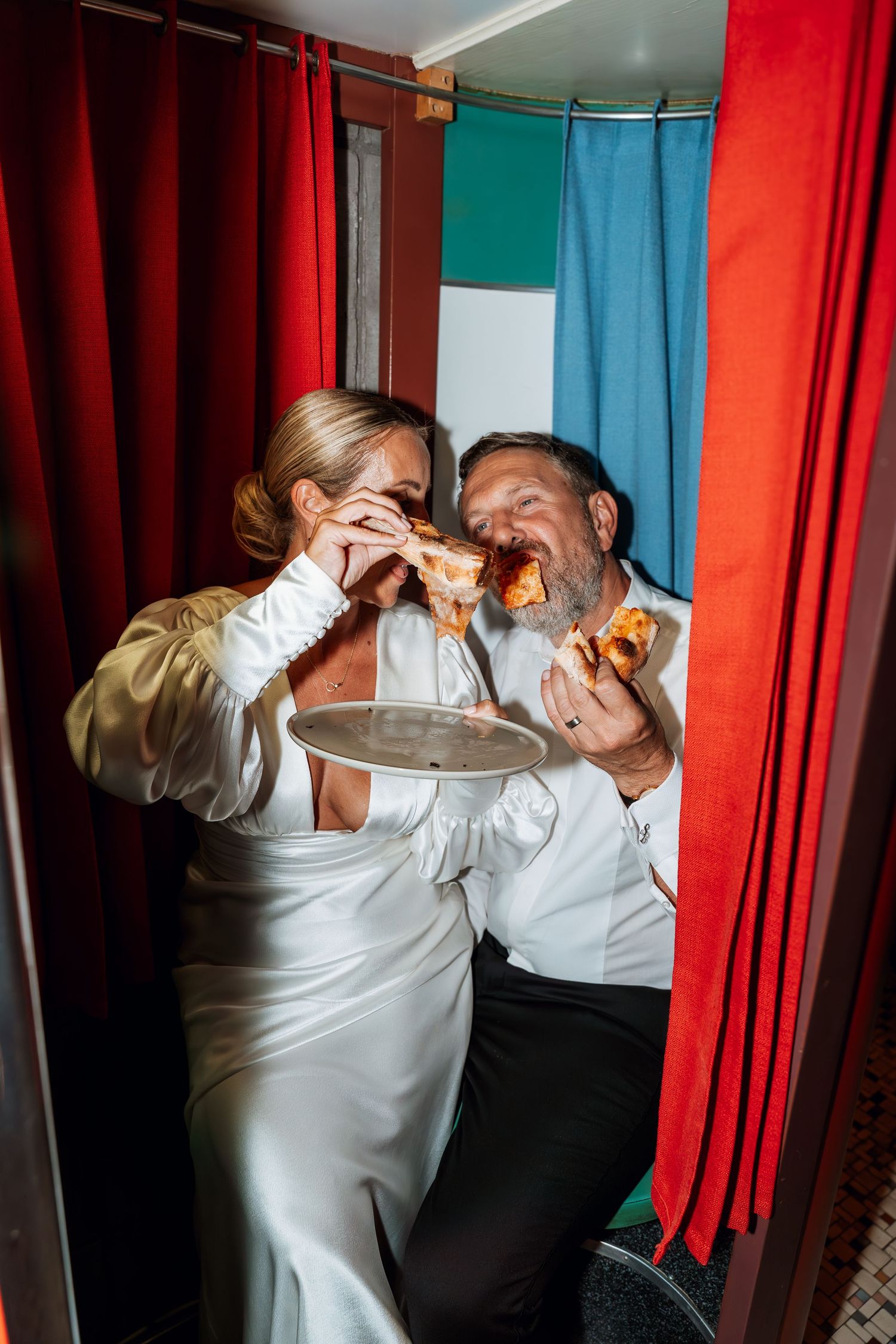 Candid dance floor moment at a wedding reception with red and turquoise curtains in the background.