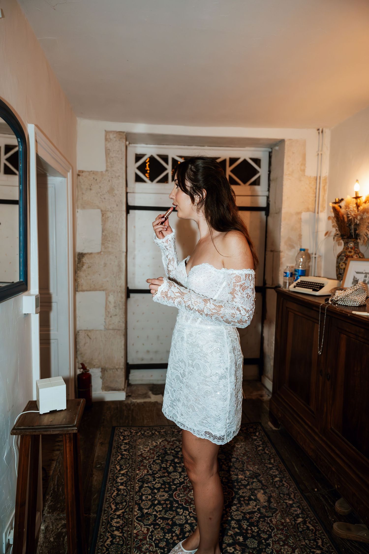 Person in white lace getting ready in a rustic stone-walled room.