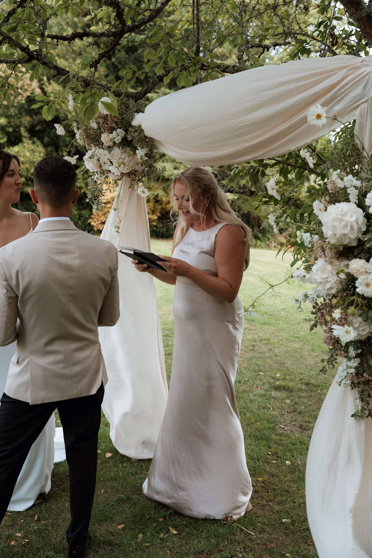 An outdoor wedding ceremony under floral archway with white draping and decorative flowers.