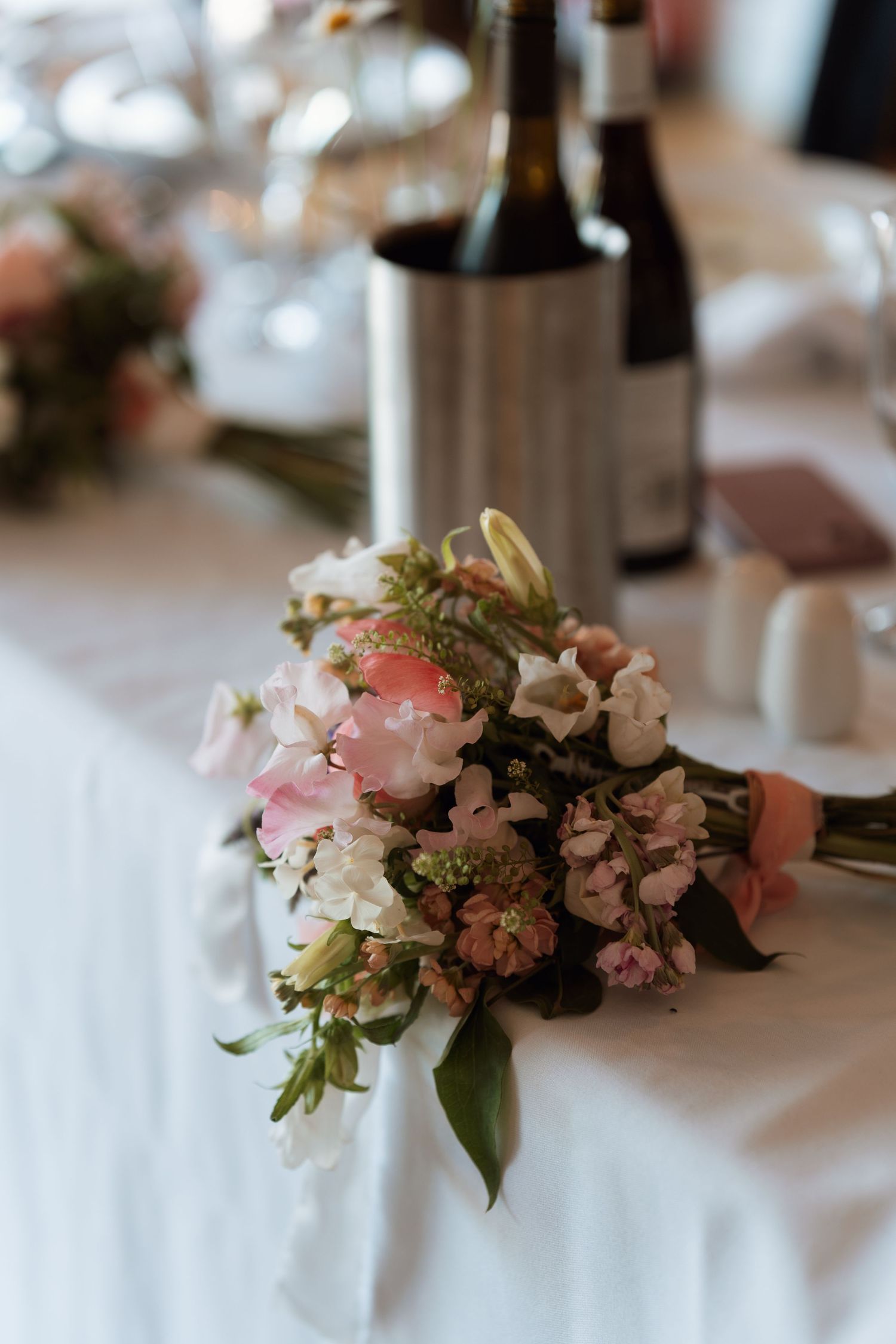 Delicate pink and white floral centerpieces on white tablecloths at wedding reception.