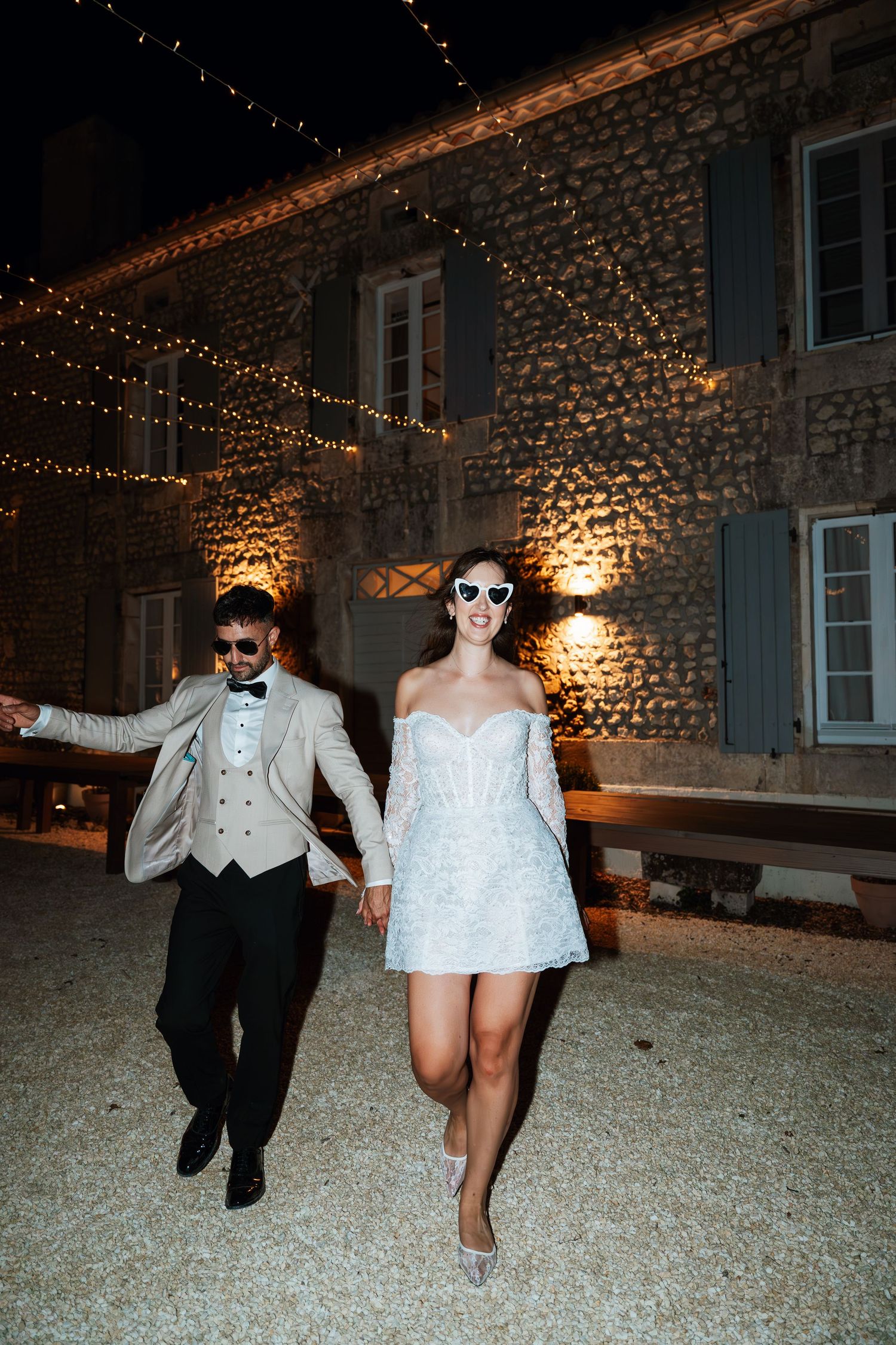 Fun nighttime wedding photos with string lights and stone wall backdrop.