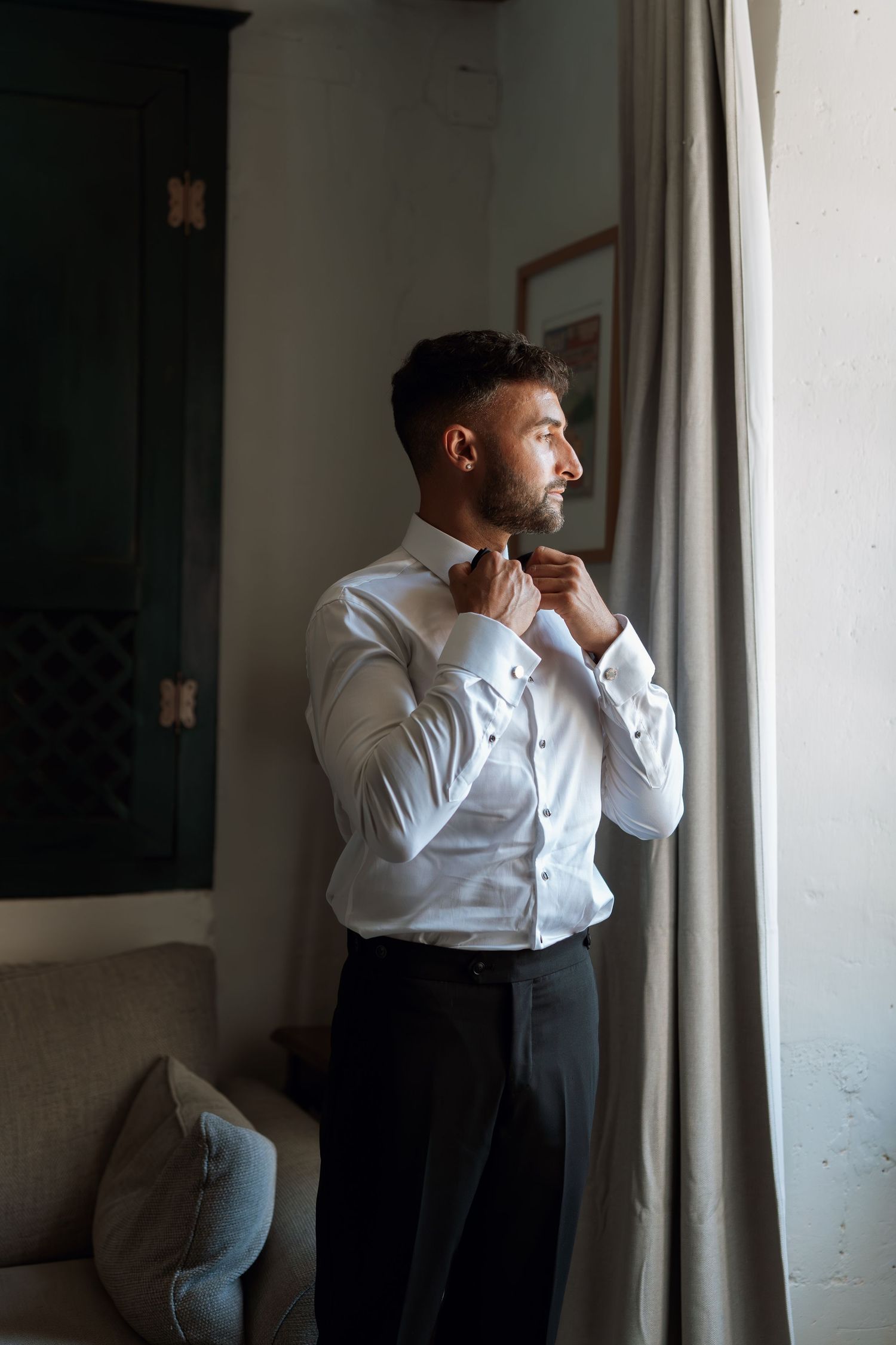 Multiple frames showing someone in formal attire adjusting their tie near a window.