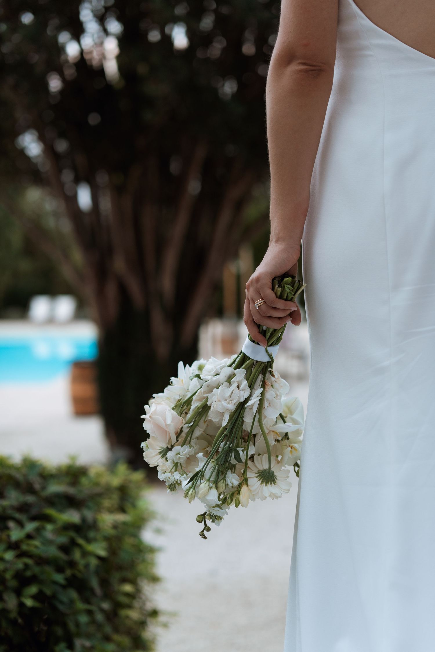 White floral bouquet against a white dress with greenery in the background.