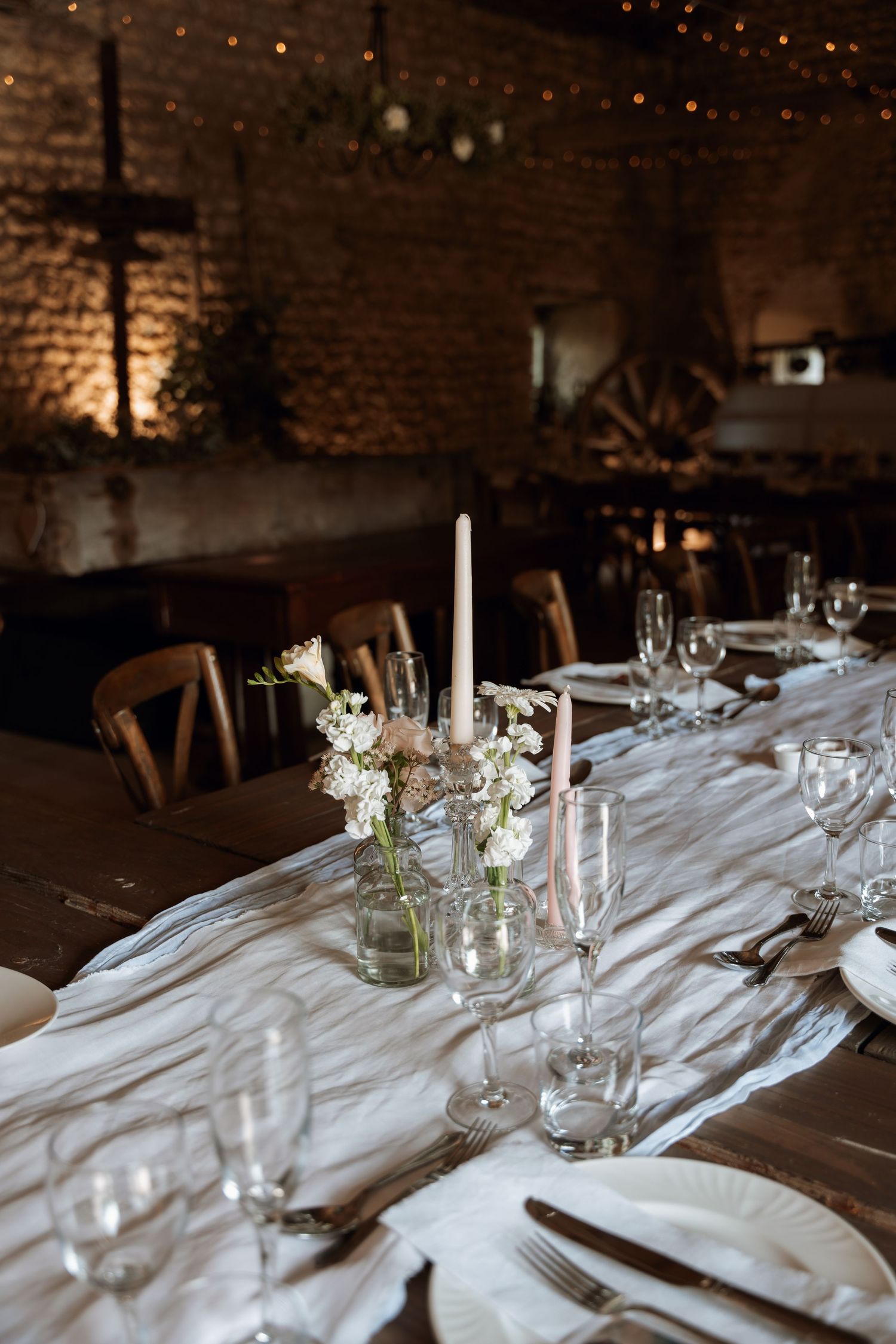 Elegant table setting with white linens, candles and floral centerpieces in rustic venue.