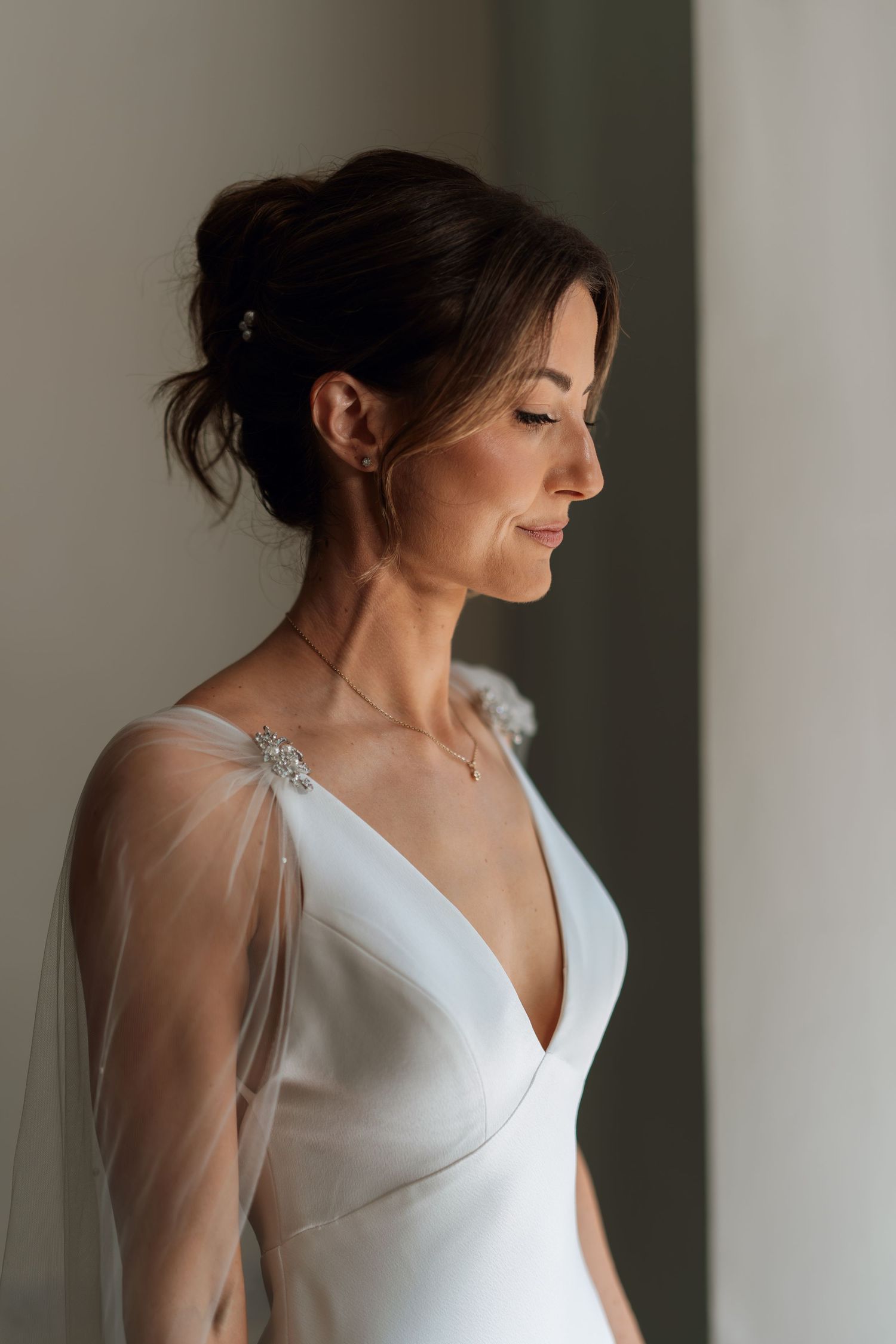 Side profile of a bride in an elegant white wedding dress with sheer sleeves and delicate neckline.