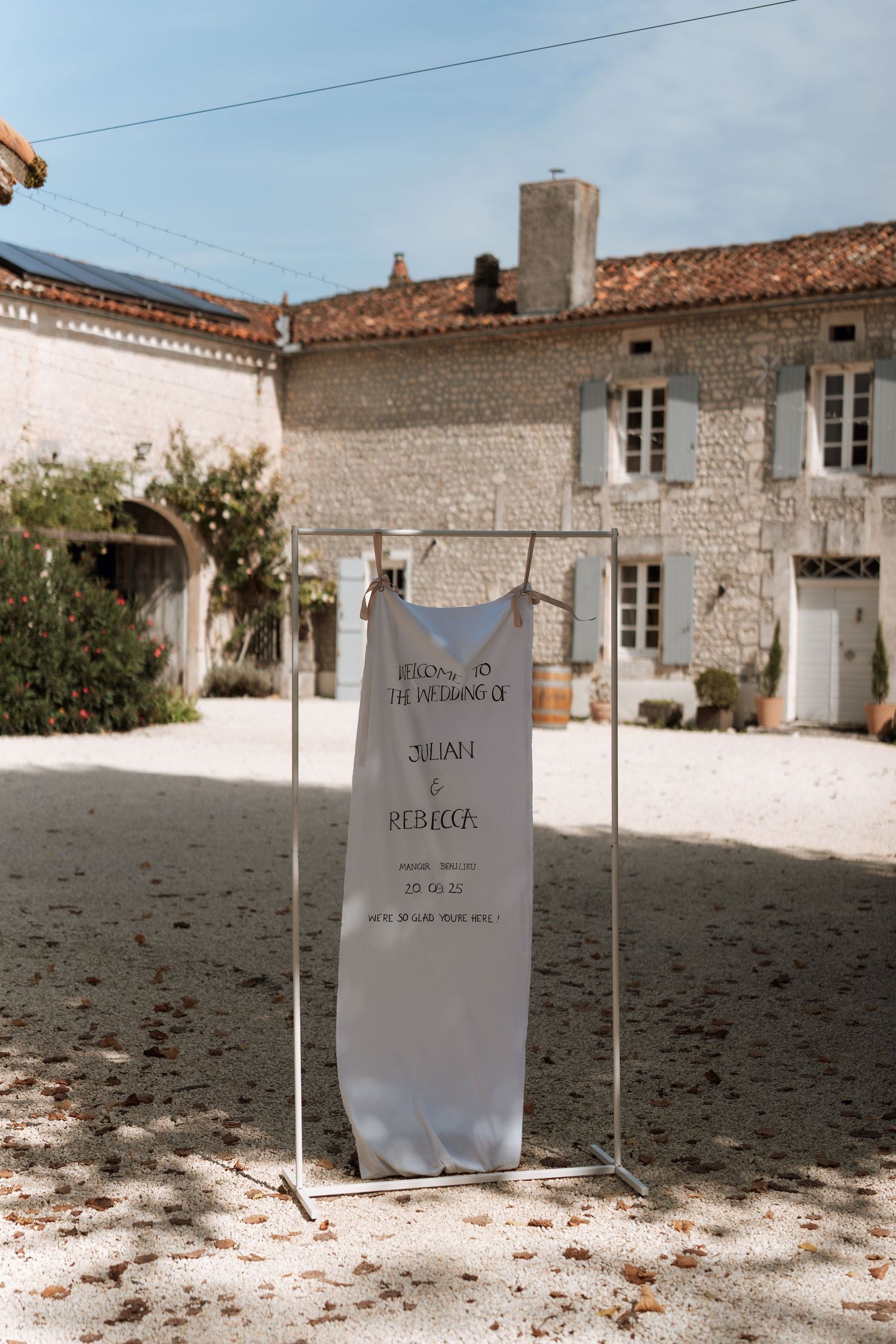 Row of white signs placed in gravel with stone building and blue shutters in background.