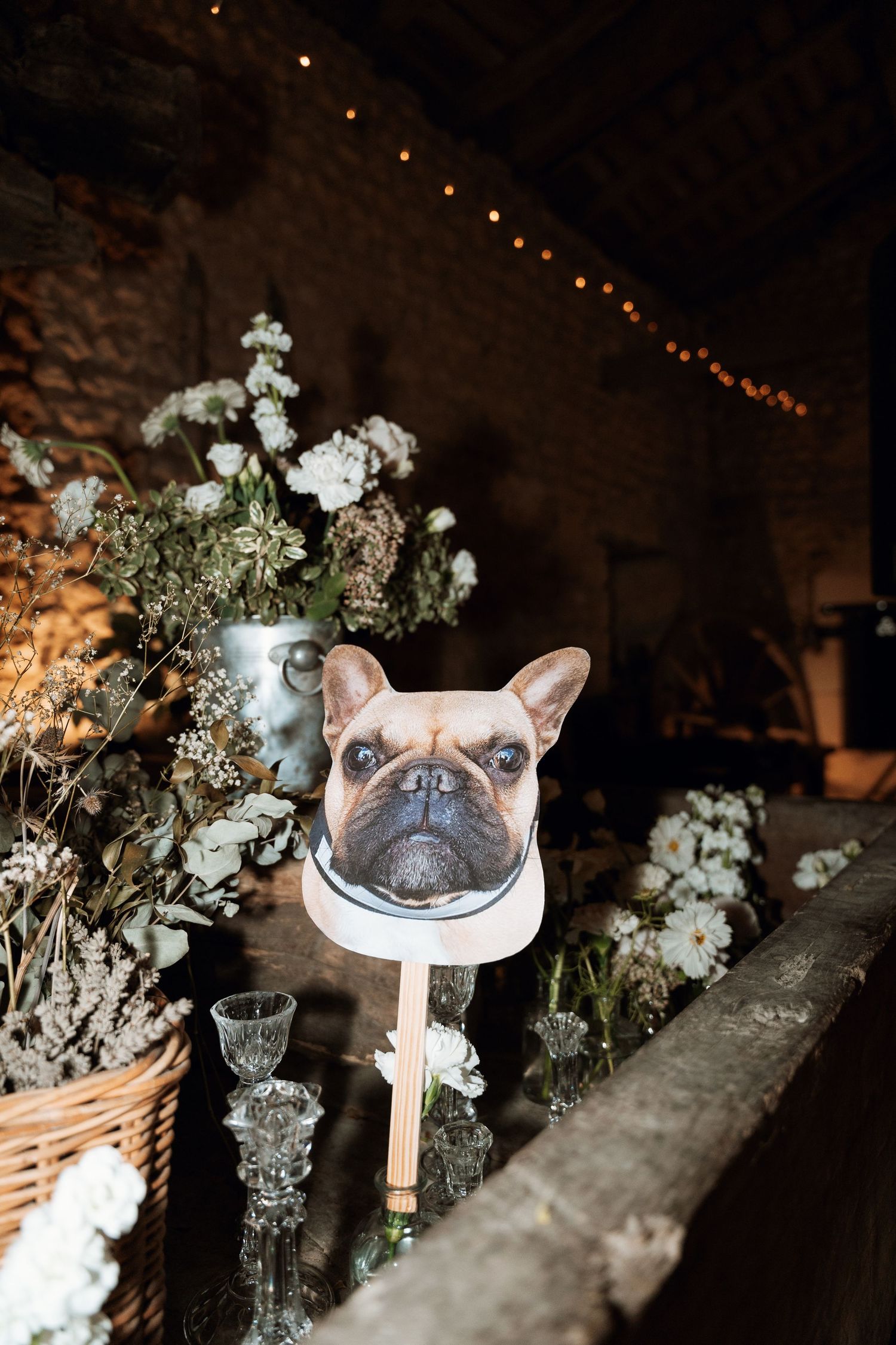French bulldog portrait displayed among white flowers and candles at wedding reception.