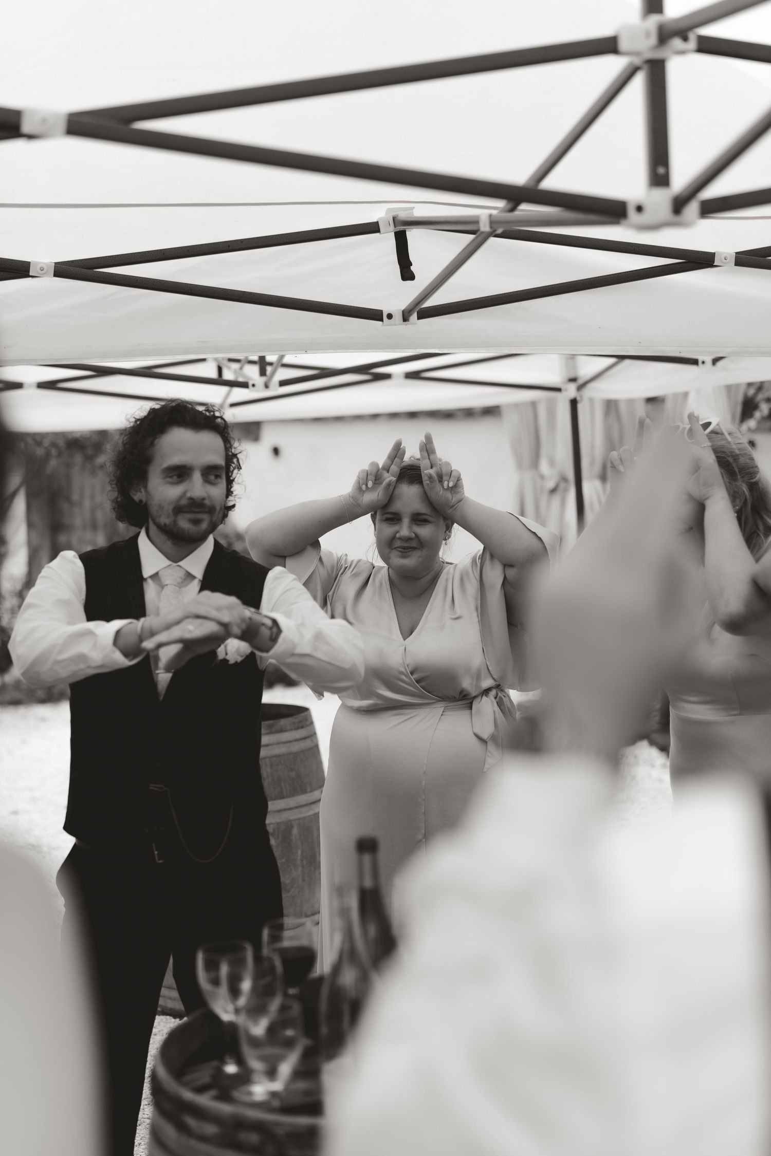 Black and white photo of wedding guests celebrating under a white tent structure.