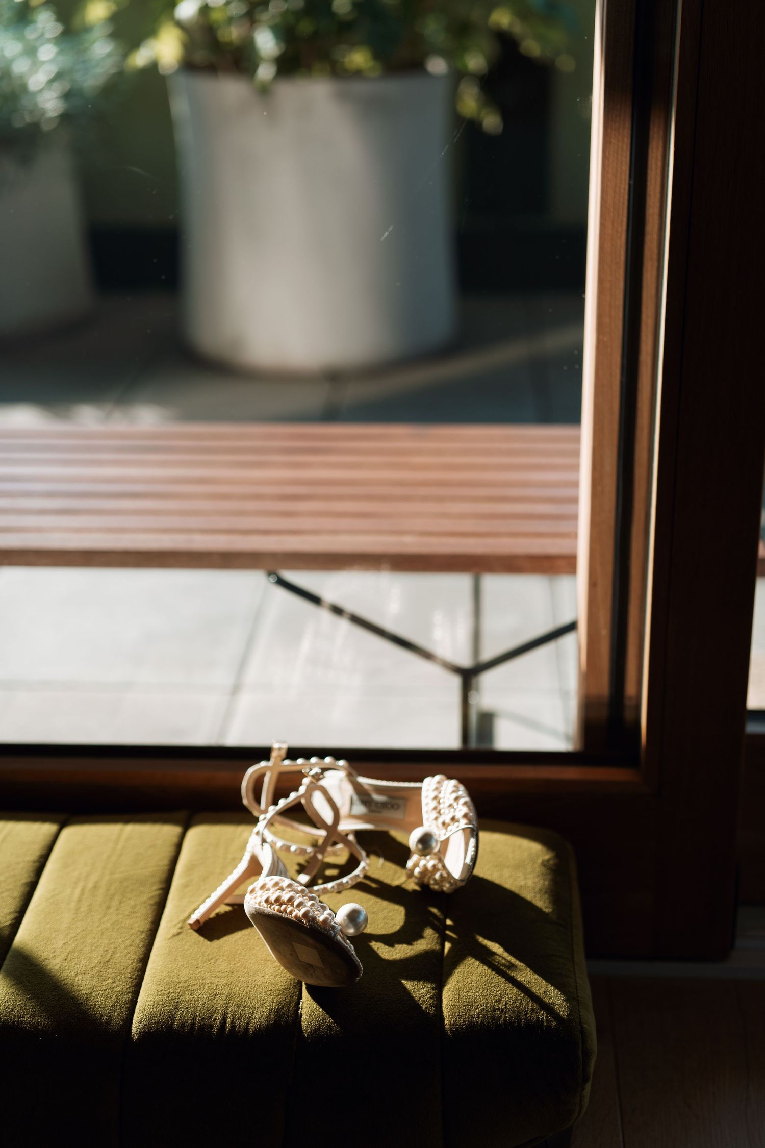 Wedding shoes resting on an olive green cushion in natural window light.