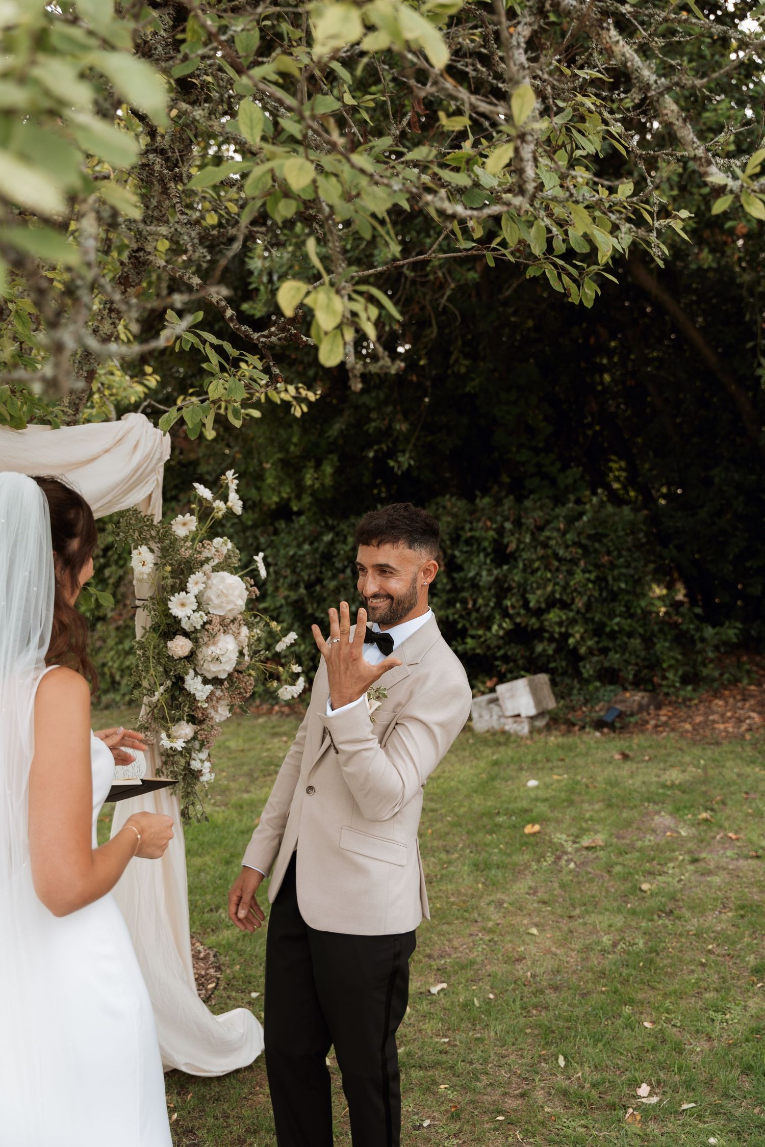 Couple shares first look moment under trees decorated with white floral arrangements and drapery.