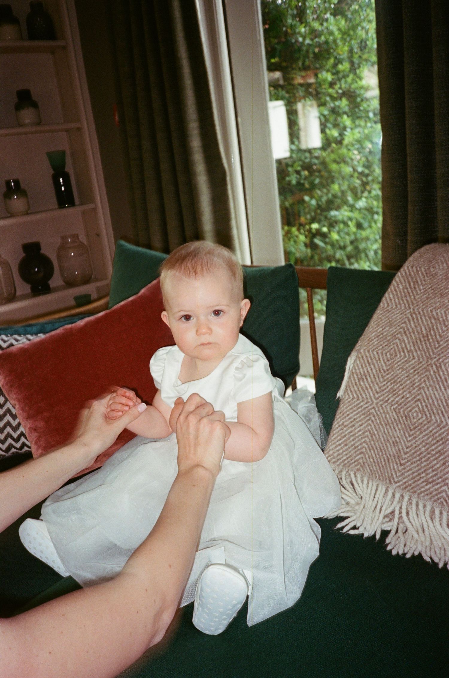 A sequence of four photos showing a baby in white clothing sitting on a dark green couch with a striped throw blanket.
