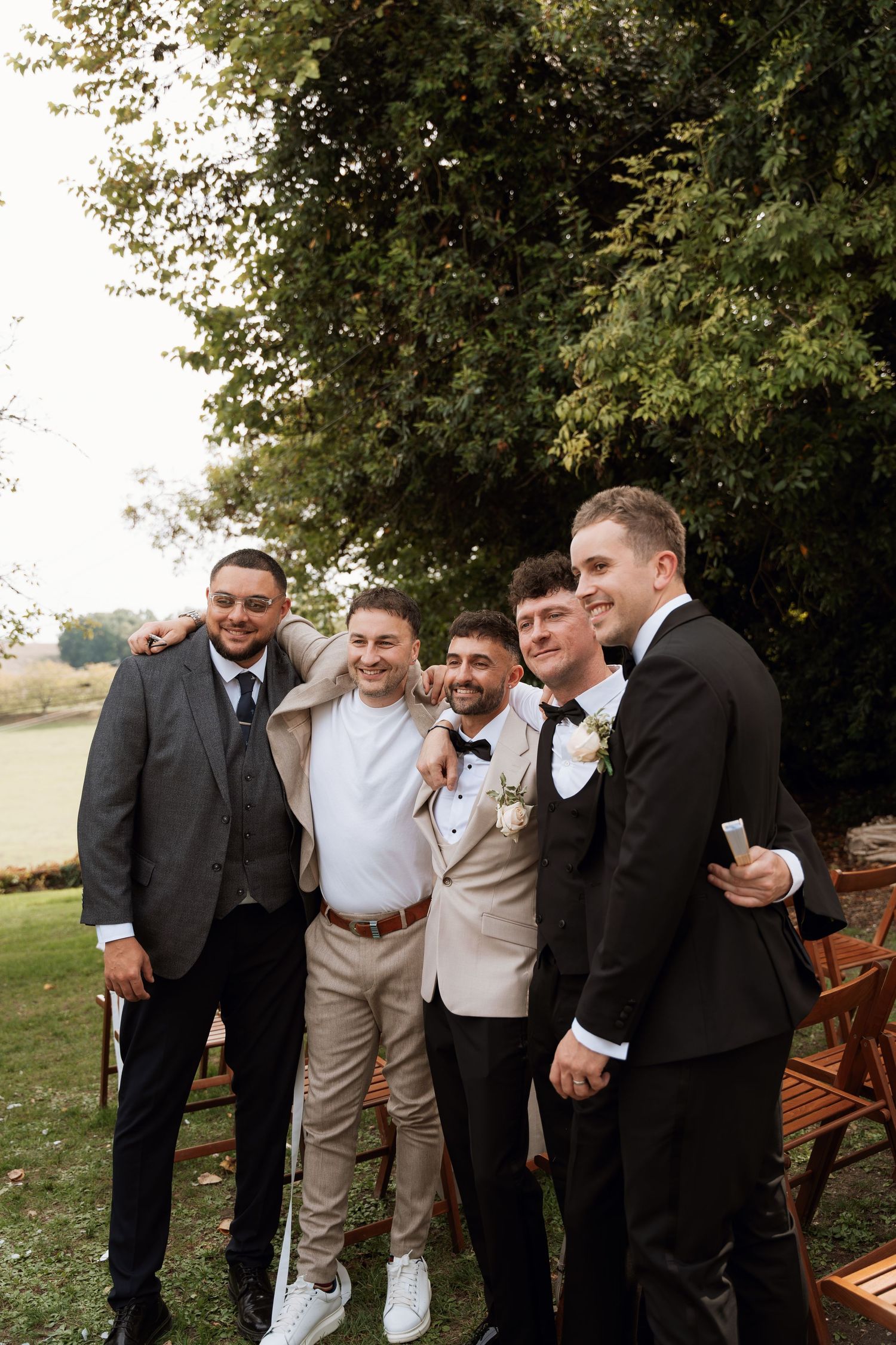 Groomsmen in formal attire sharing laughs together outdoors during wedding festivities.