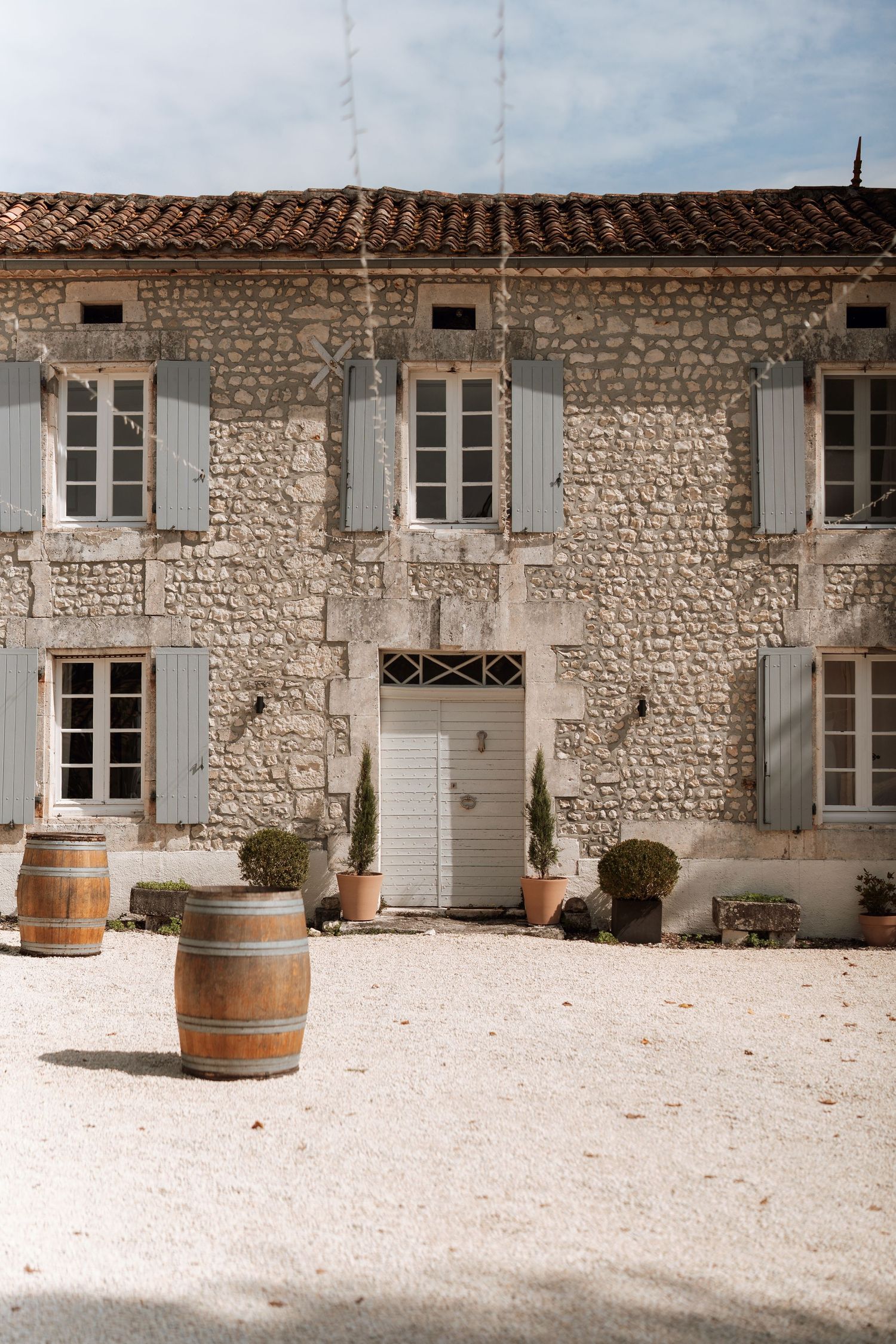 Stone farmhouse with blue shutters and wooden barrels in rustic courtyard.