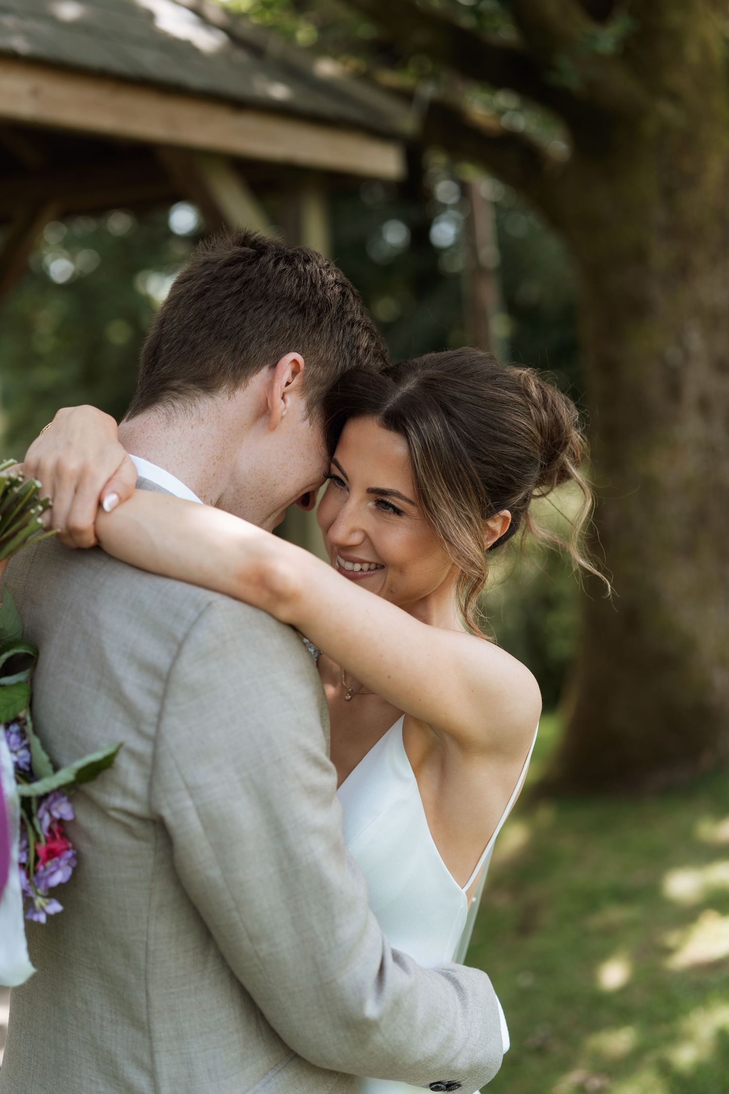 A romantic moment captured between newlyweds embracing during an outdoor garden wedding celebration.