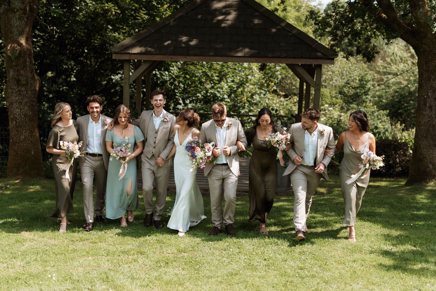 Wedding party poses together on a grassy lawn wearing coordinated beige and white attire.
