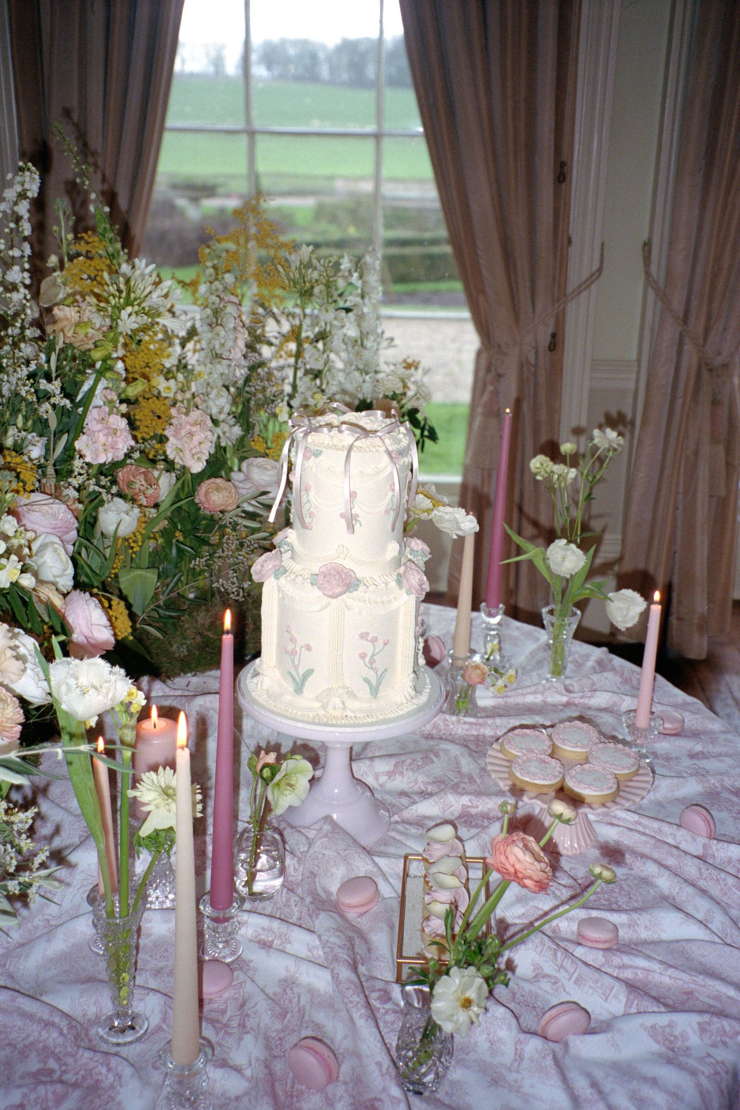 Elegant wedding reception table with pink and white floral arrangements, candles, and tiered white cake on lace tablecloth.