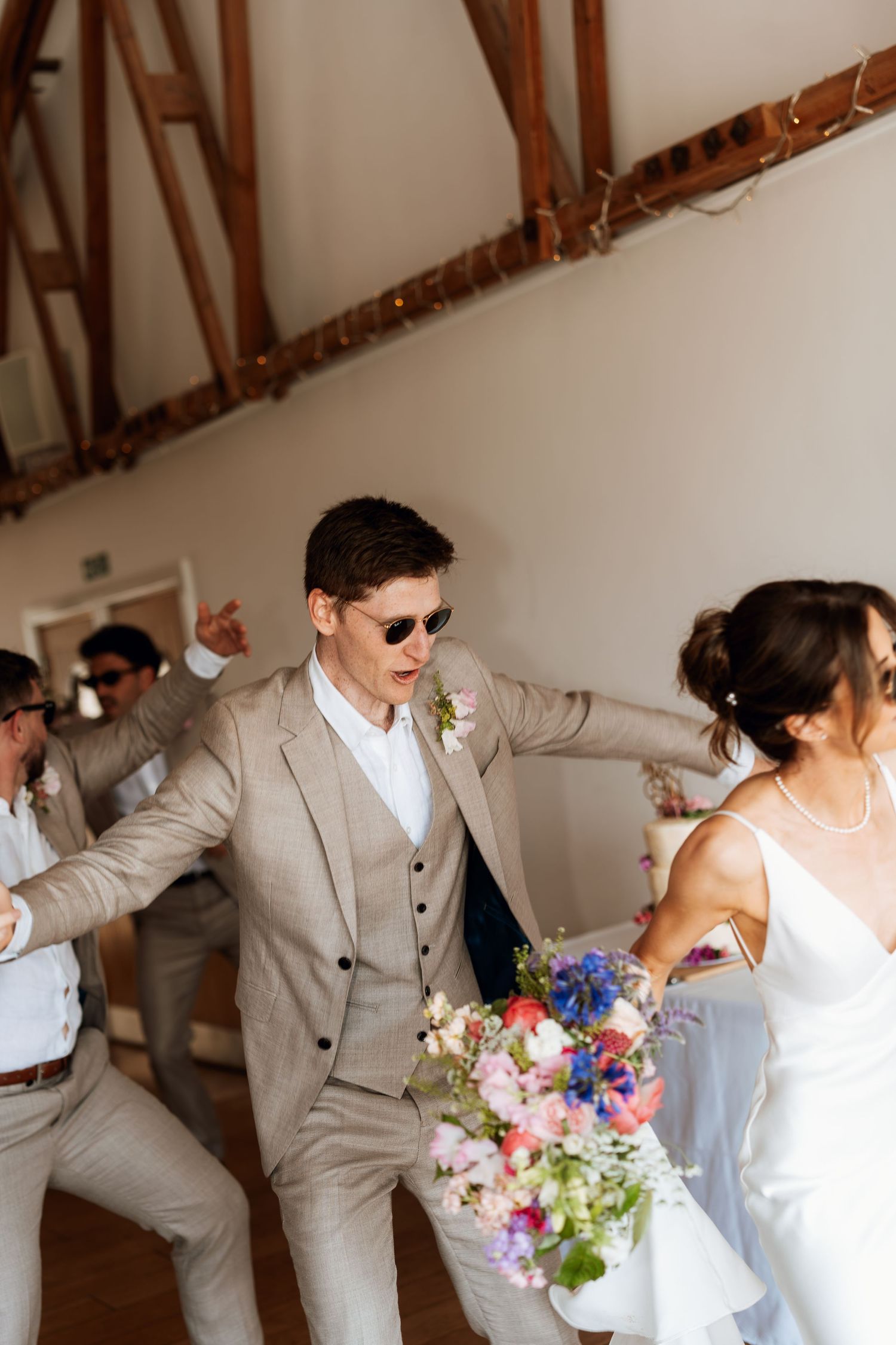 Wedding couple dancing and celebrating with joy in a rustic venue with exposed wooden beams.