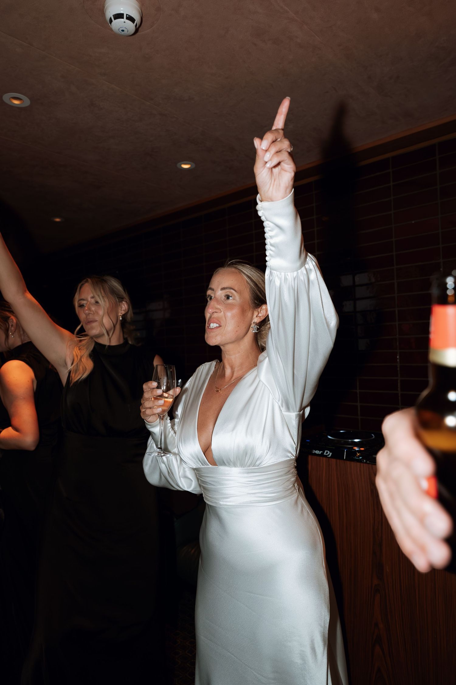 A person in white dancing with raised arms at a dimly lit celebration.