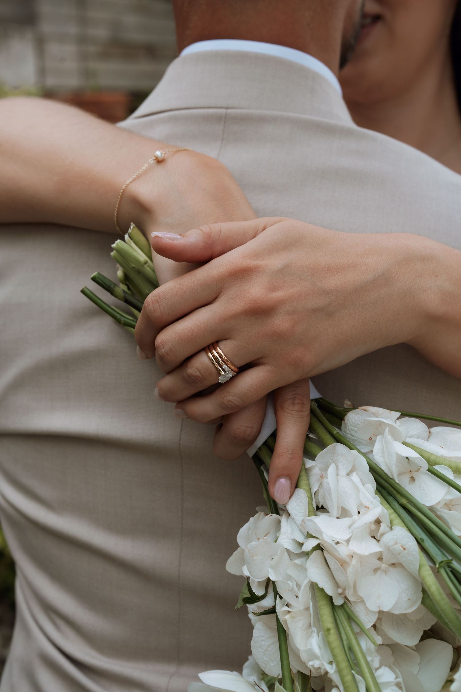 Close-up of hands holding white flowers and showing off wedding rings.