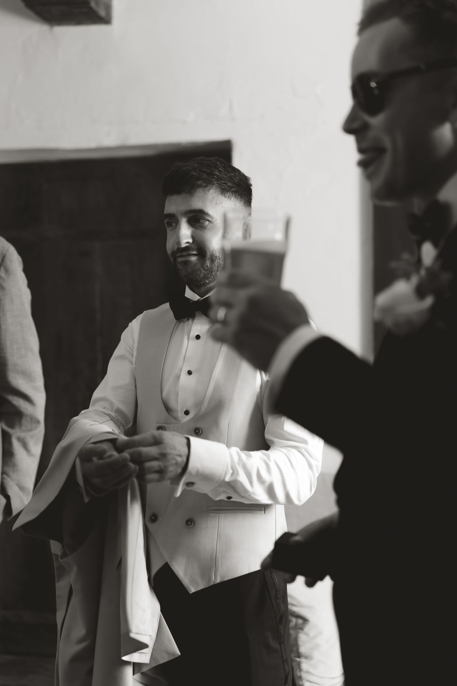 Men in formal white tuxedos and suits gathered indoors in black and white photograph.