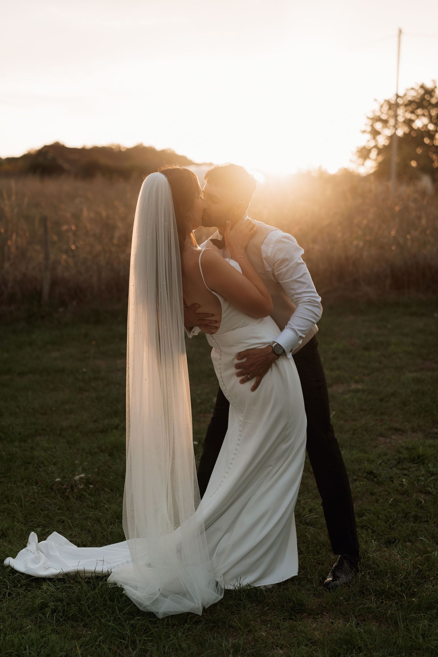 A romantic sunset dip pose with flowing white wedding dress in a field.