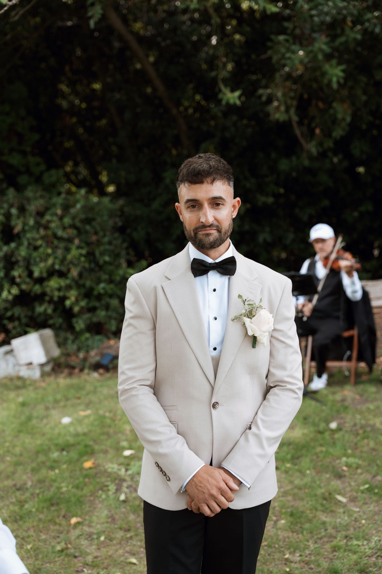 Groomsmen in cream colored tuxedo jackets and black bow ties pose for formal wedding photos outdoors.