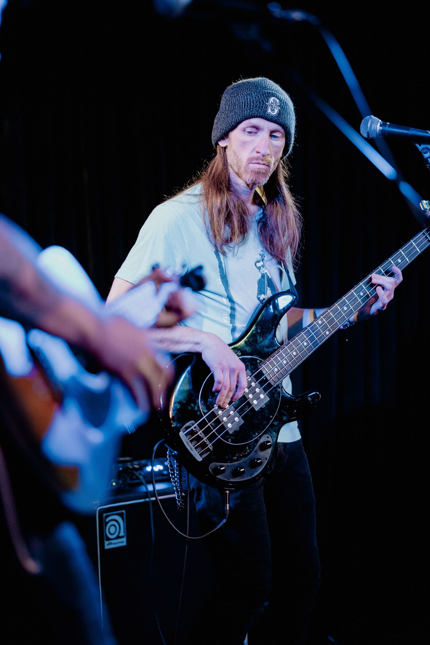 Live music portrait of bassist on stage with blue lighting and performance focus.