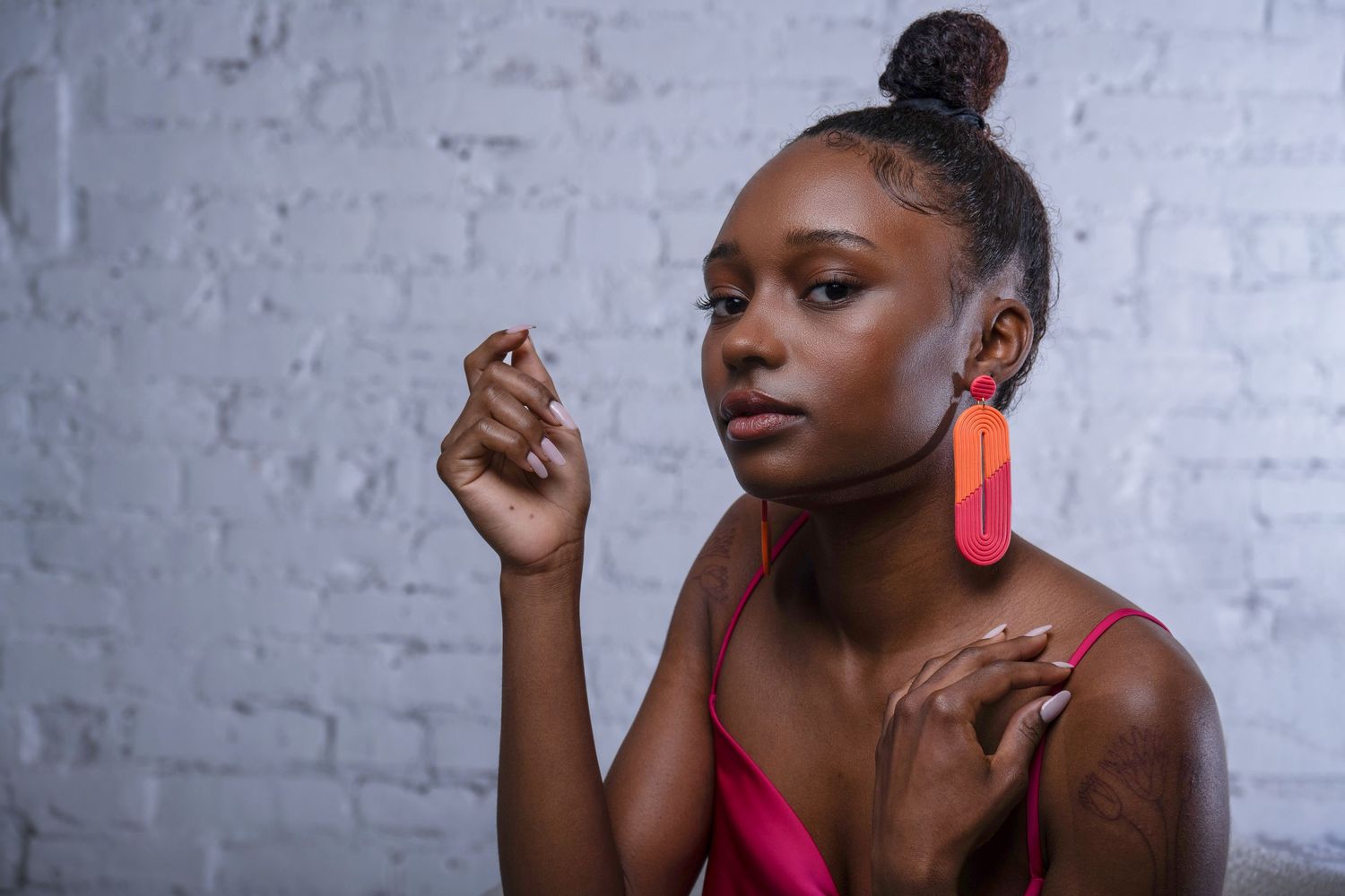 Studio portrait of model wearing bold geometric earrings and white textured blouse, modern fashion look.