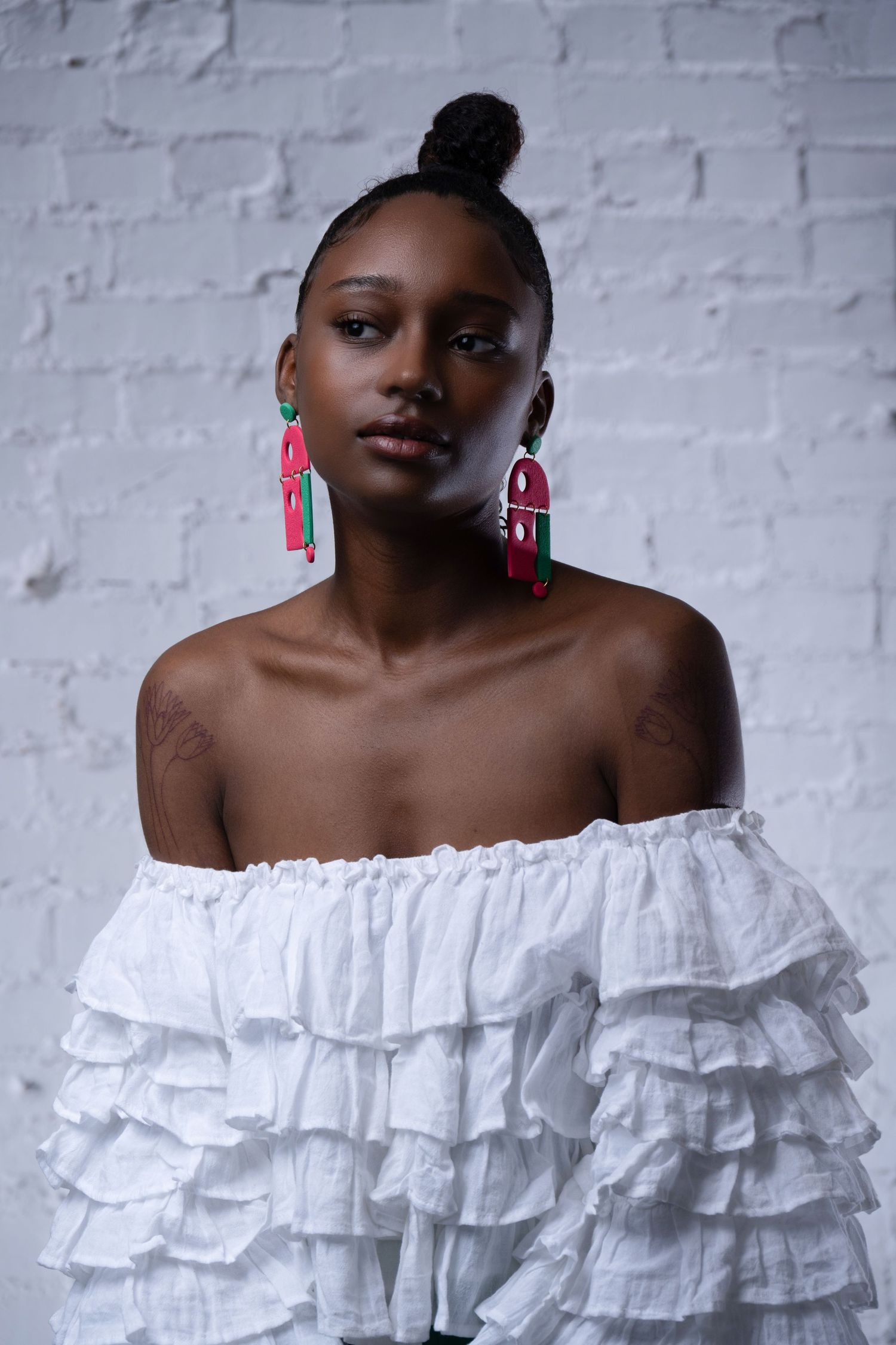 Fashion portrait of model in white ruffled top with statement earrings against textured brick wall.