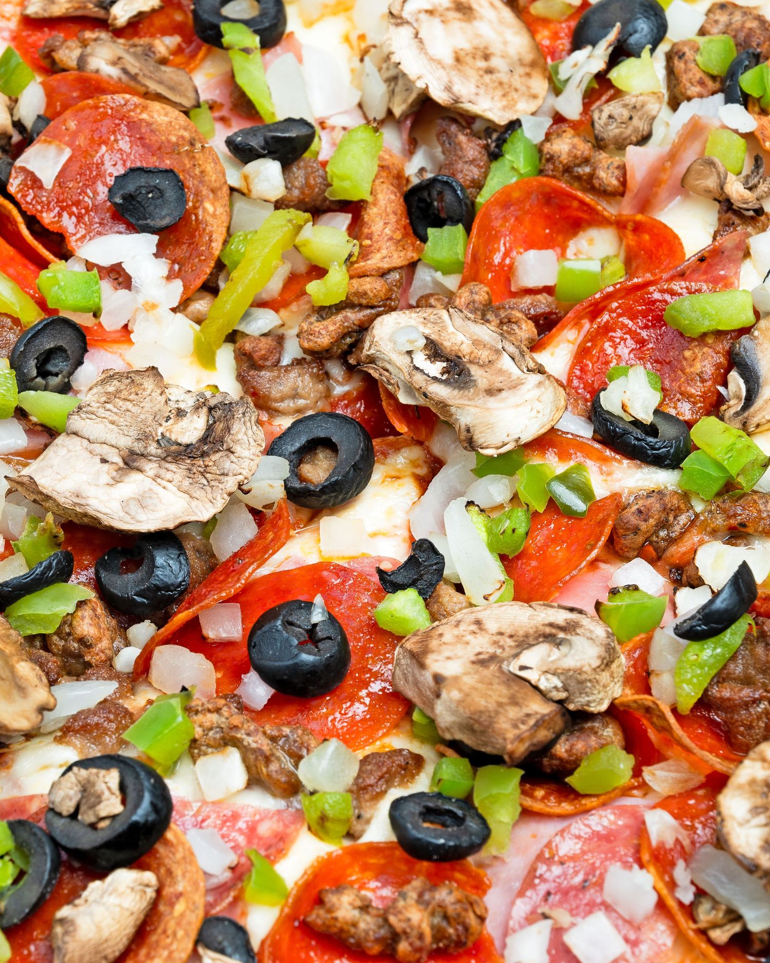 Close-up of loaded supreme pizza with pepperoni, sausage, mushrooms, olives and green peppers on melted mozzarella.