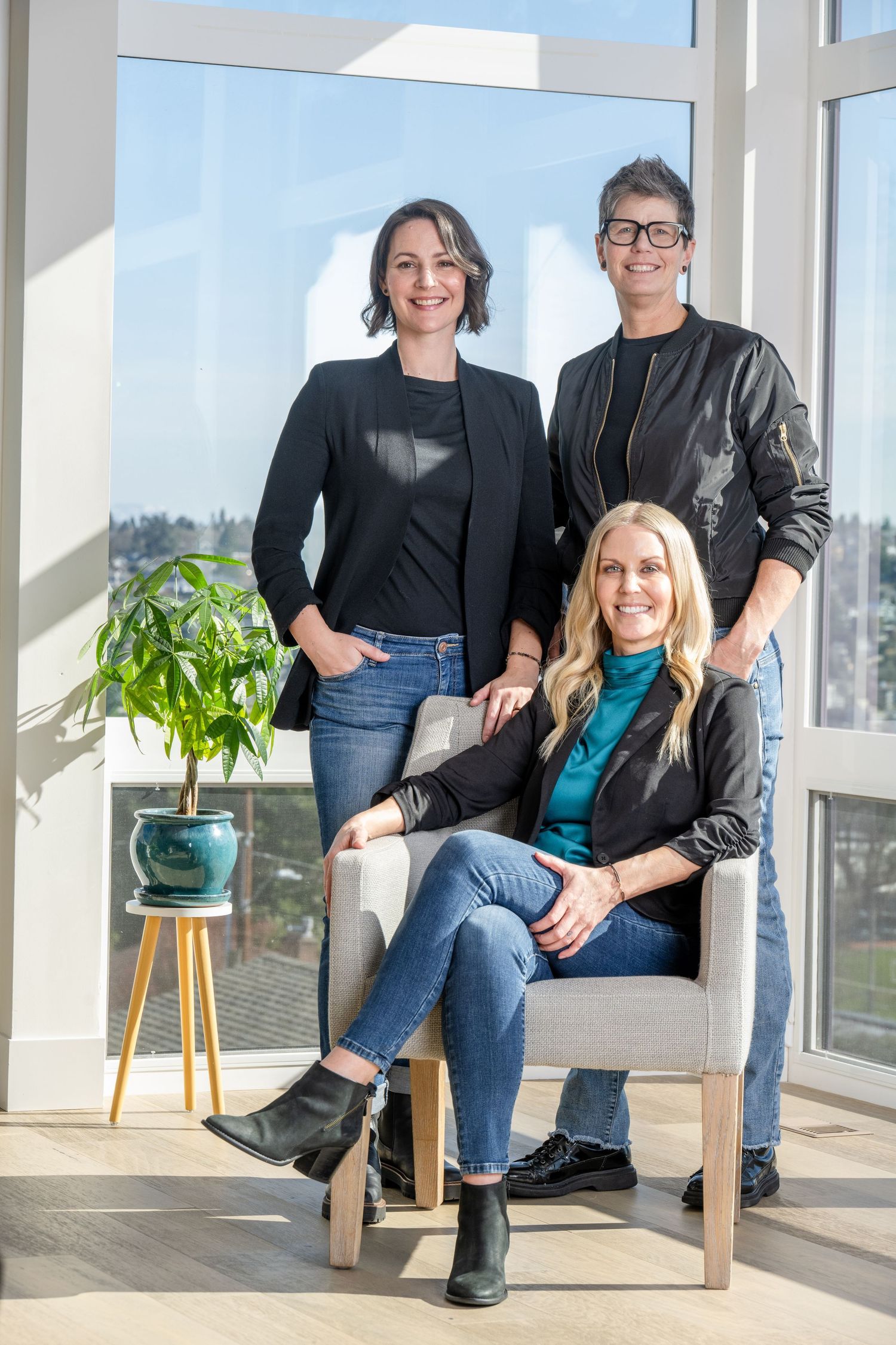 Team portrait of three women in modern office setting, photographed in natural light for corporate branding and leadership profiles.