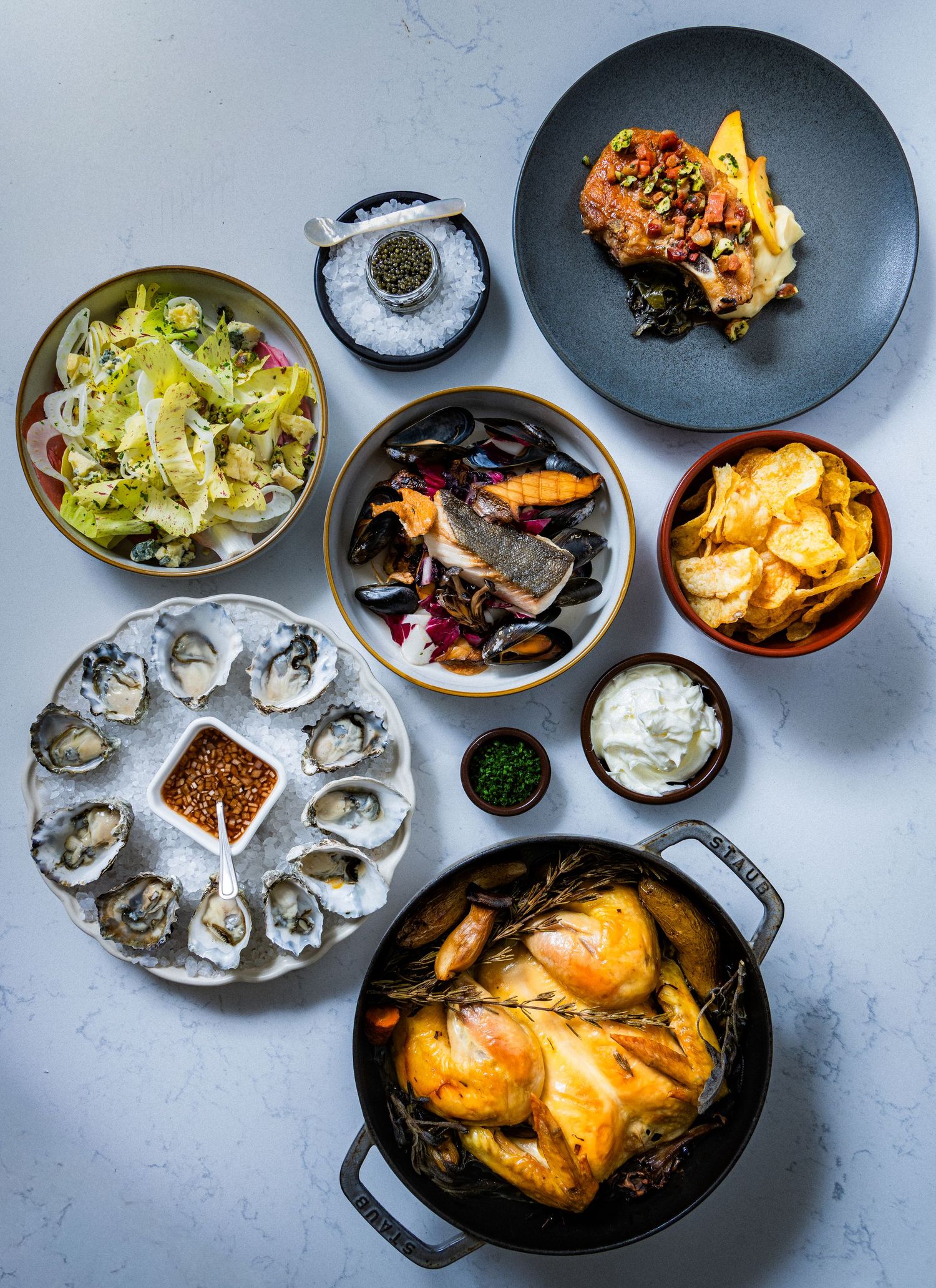 Overhead food spread with oysters, roast chicken, and sides, photographed for restaurant menu and editorial use.