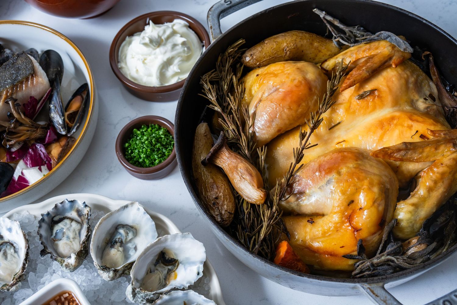 Overhead spread with roast chicken, oysters, and sides, photographed for restaurant menu and editorial food use.