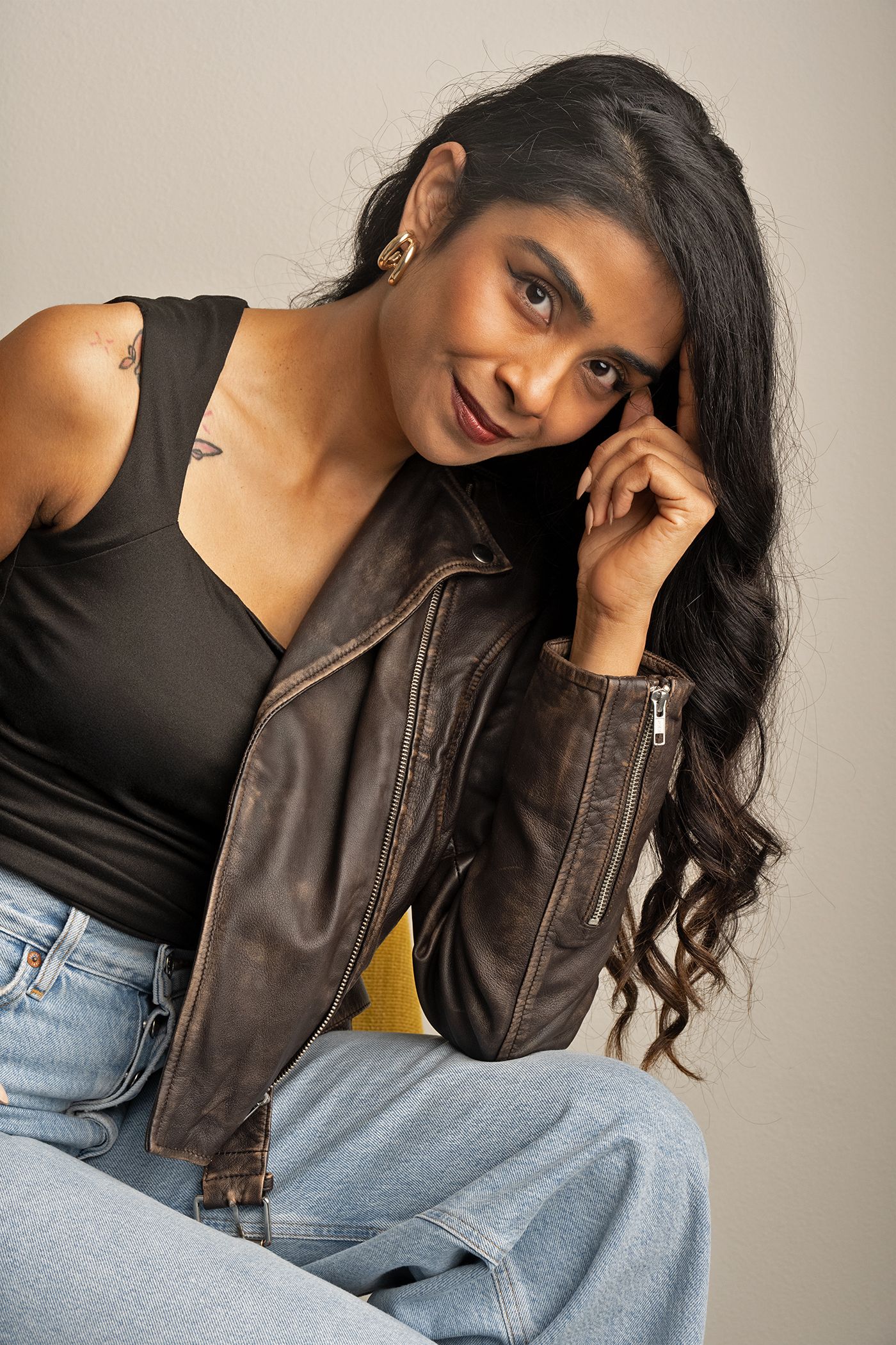 Studio portrait of woman in leather jacket, confident pose with modern minimalist backdrop.