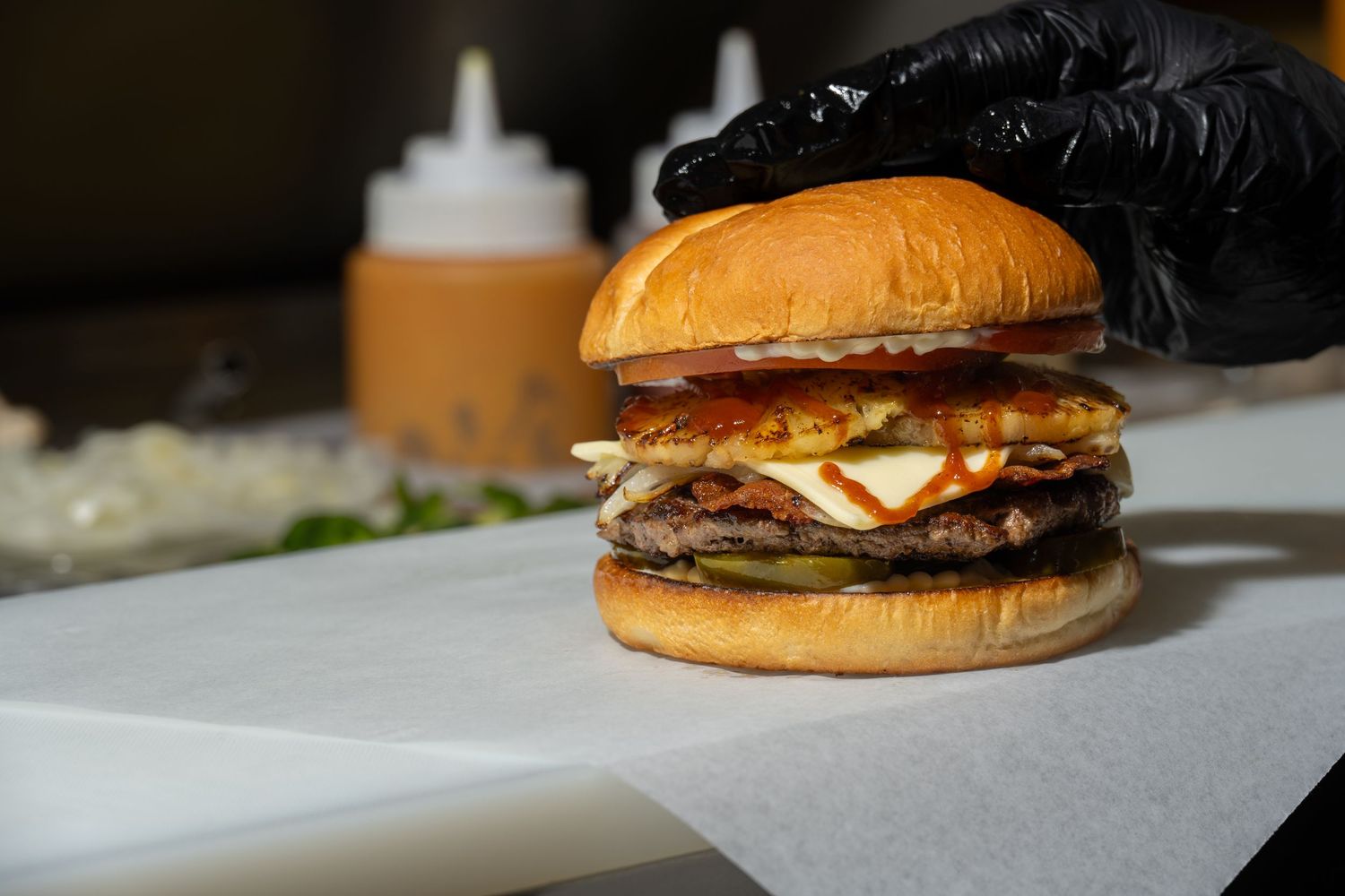 Gourmet burger with grilled pineapple, bacon, melted cheese and pickles styled for commercial food photography.