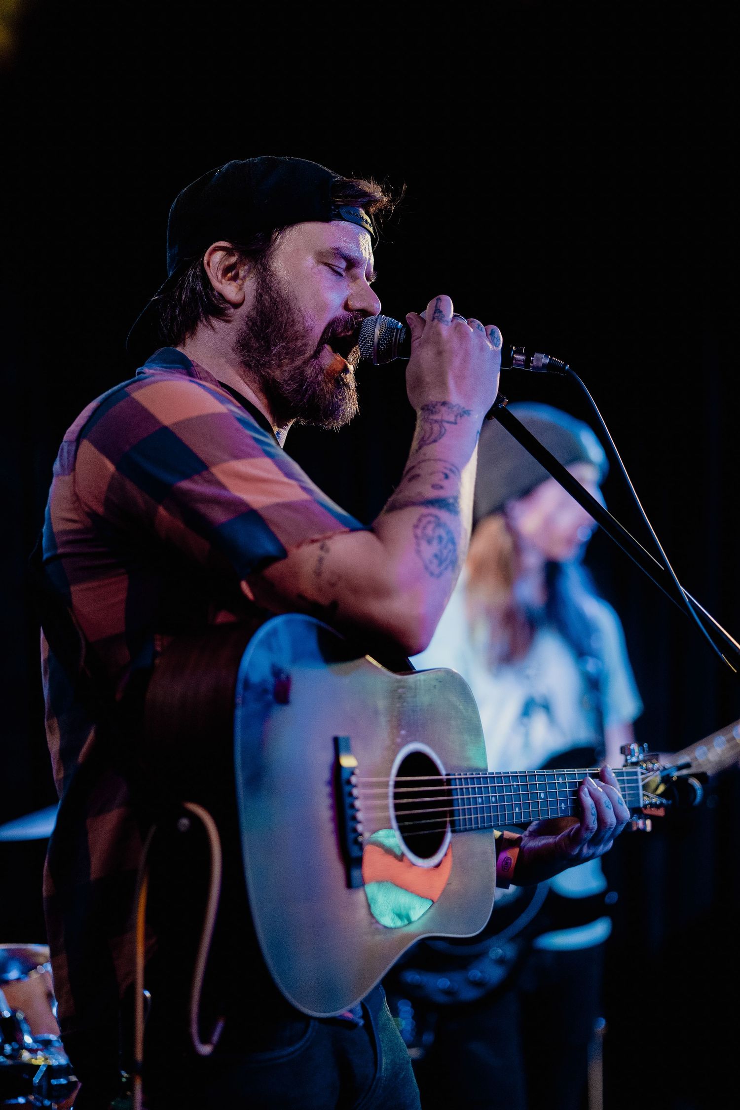Singer-songwriter performing on stage with acoustic guitar under dramatic concert lighting.