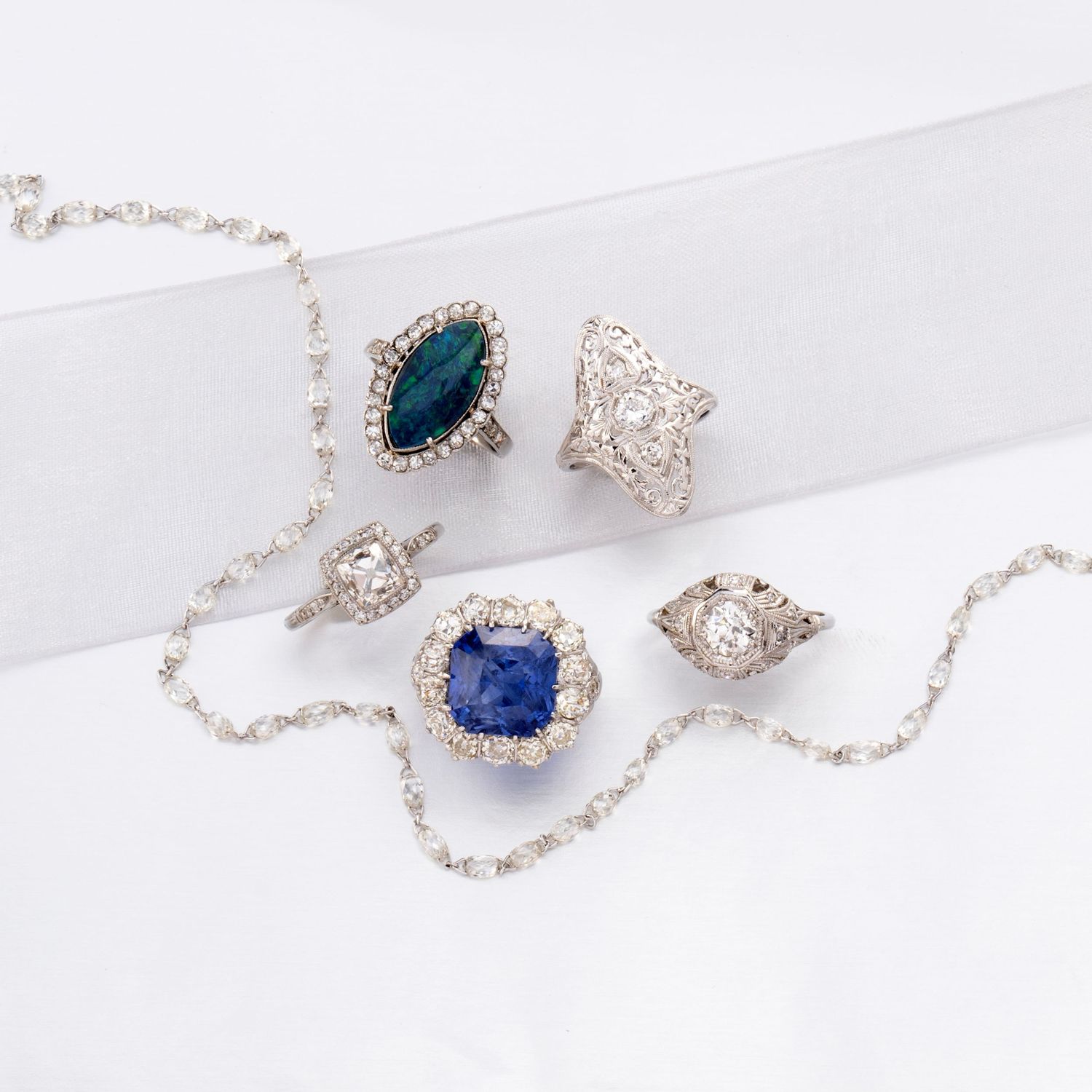 Vintage diamond rings and sapphire jewelry styled on white fabric with soft light and refined editorial composition.