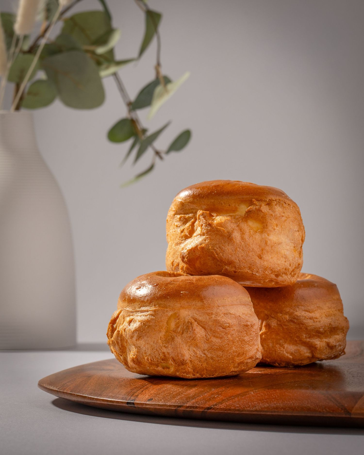 Freshly baked Persian cream puffs brioche buns stacked on wooden board, photographed for bakery branding and commercial use.