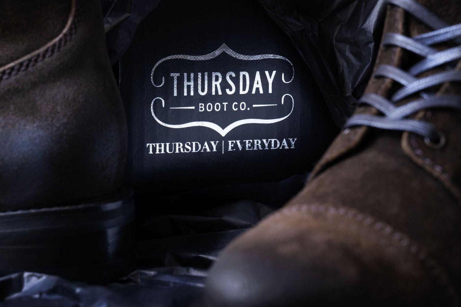 Thursday Boot Co. logo detail photographed between leather boots for footwear branding and lifestyle marketing.