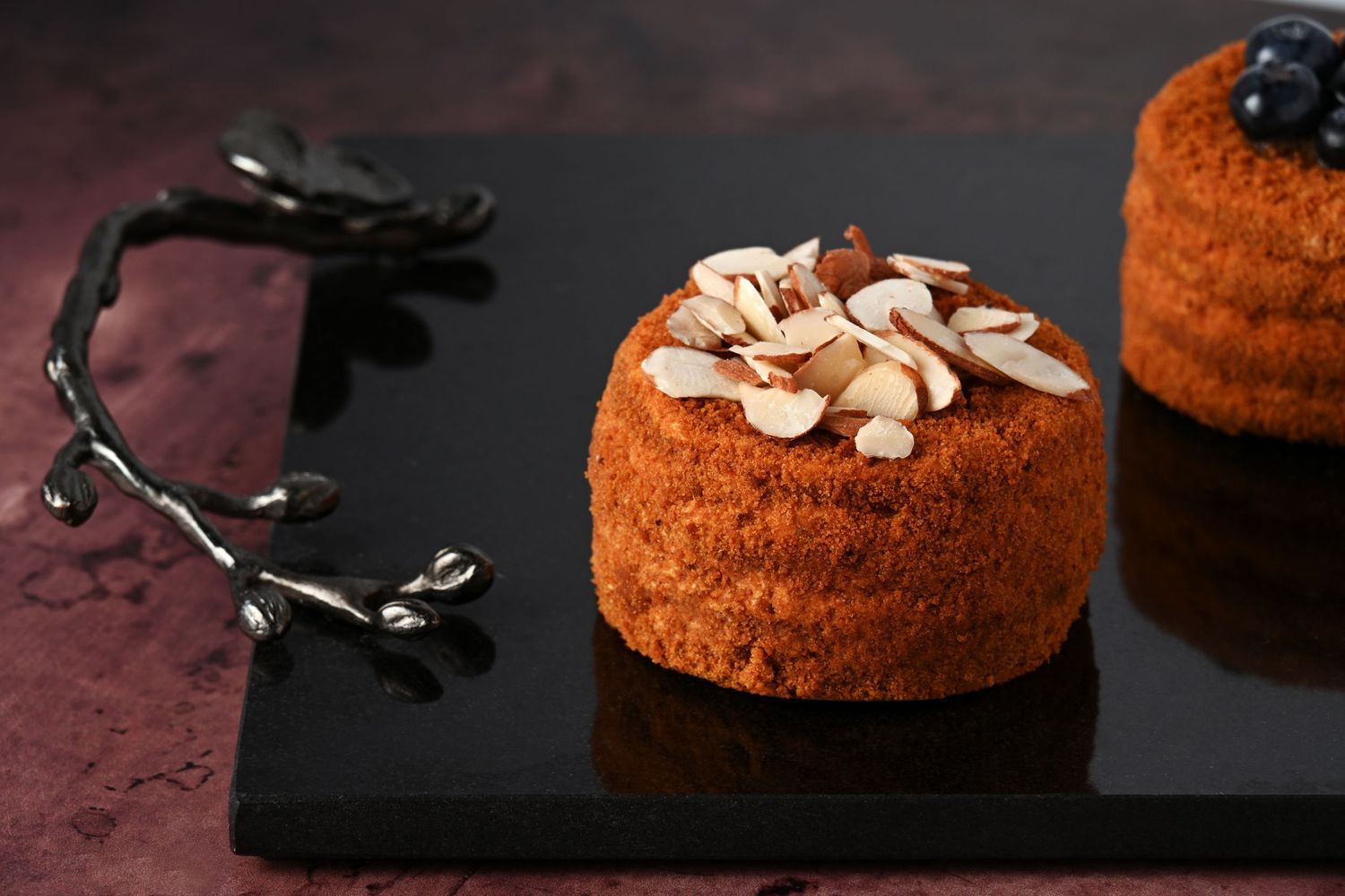 Mini cake topped with sliced almonds, styled with dramatic lighting for bakery branding and dessert photography.