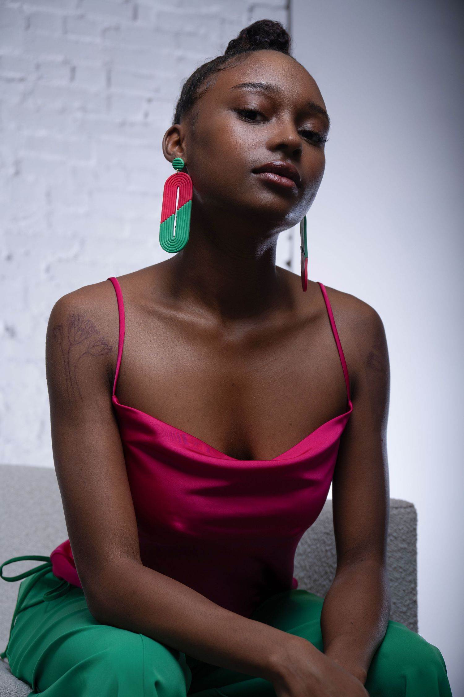Editorial portrait with vibrant red and green statement earrings, contemporary fashion styling.